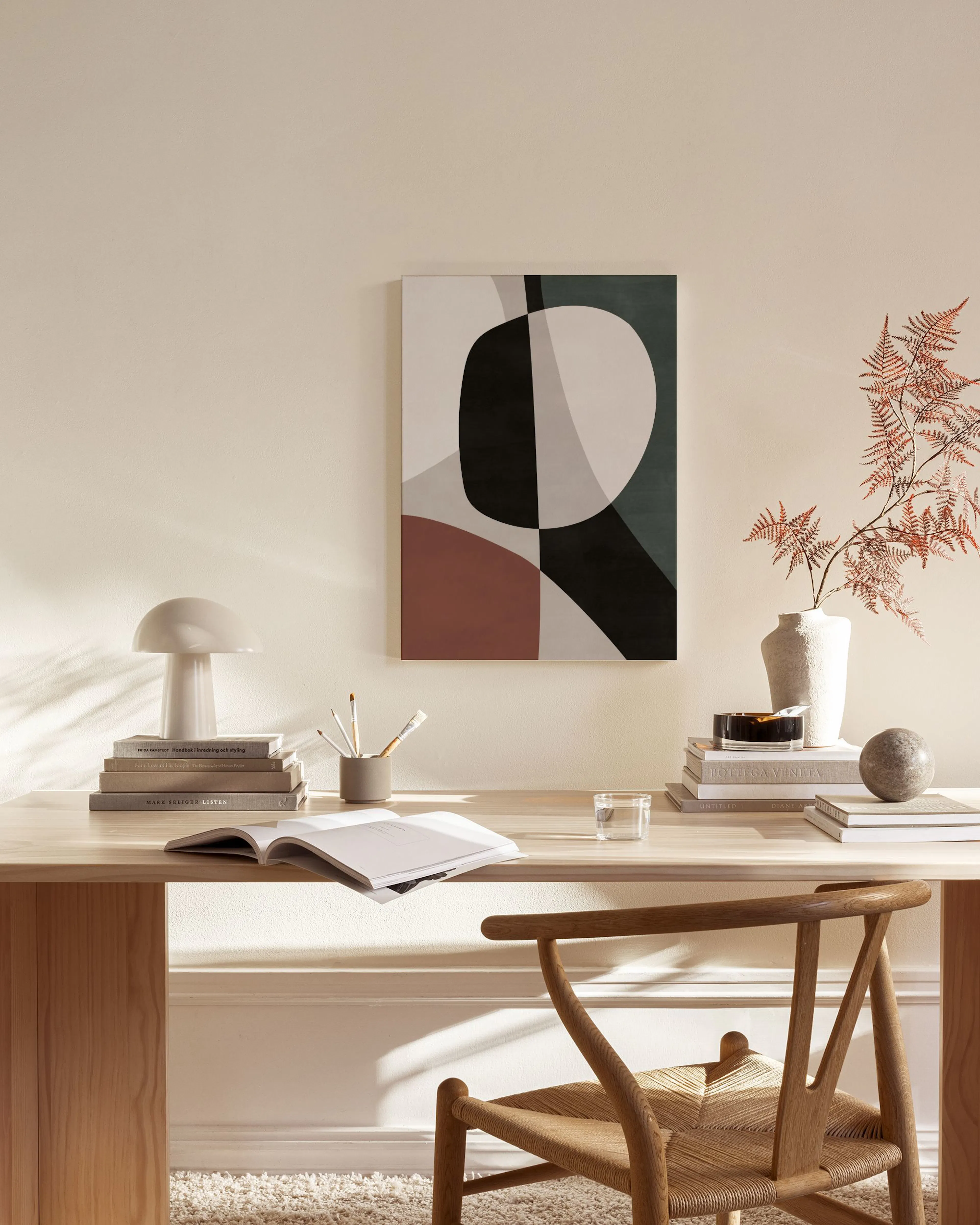 Leinwandbild mit abstrakten Formen in Schwarz, Beige, Grün und Rotbraun, an einer hellen Wand über einem Sideboard.