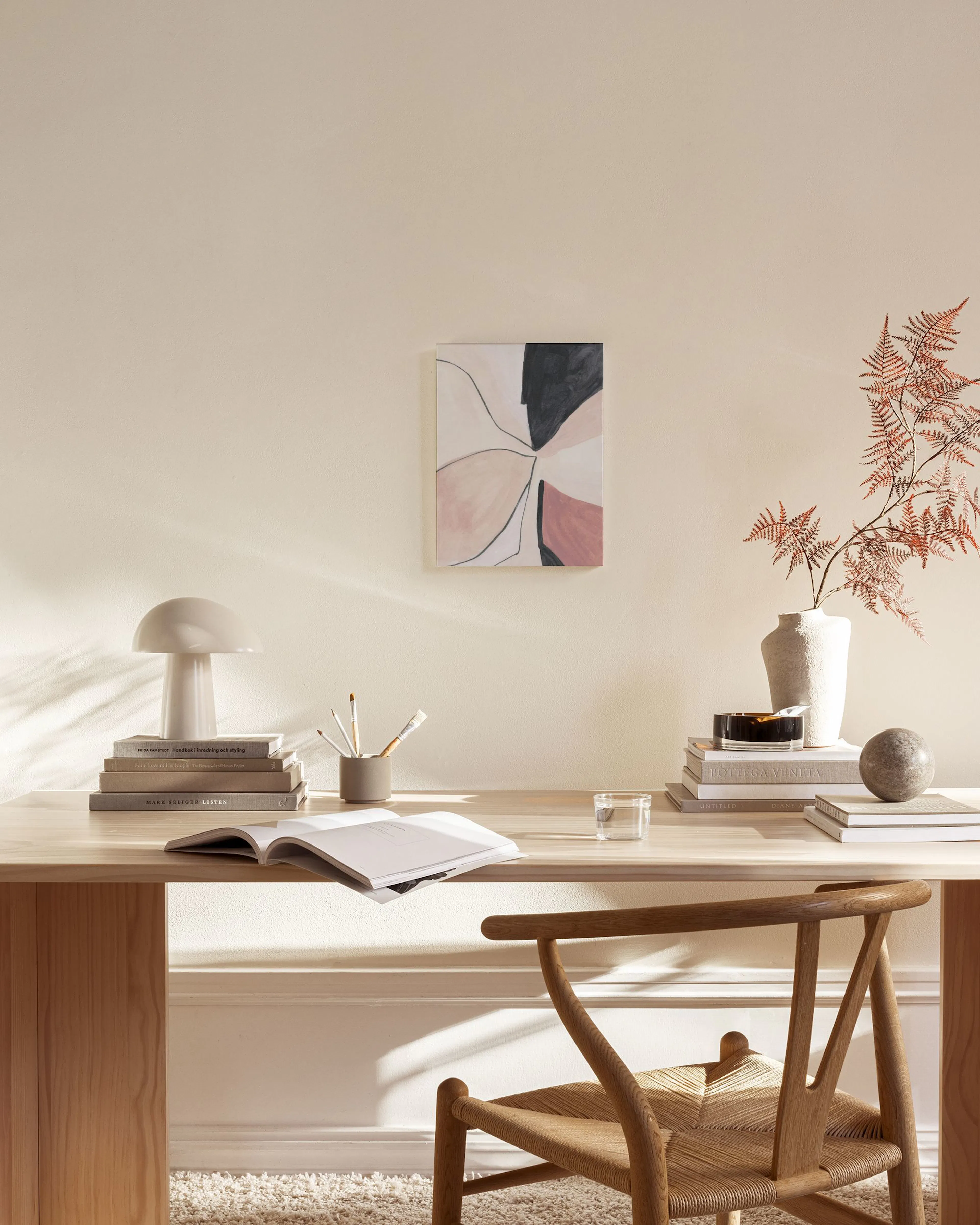 Canvastavla med abstrakta former i svart, rosa och beige, hängande i ett ljust vardagsrum över en bänk.