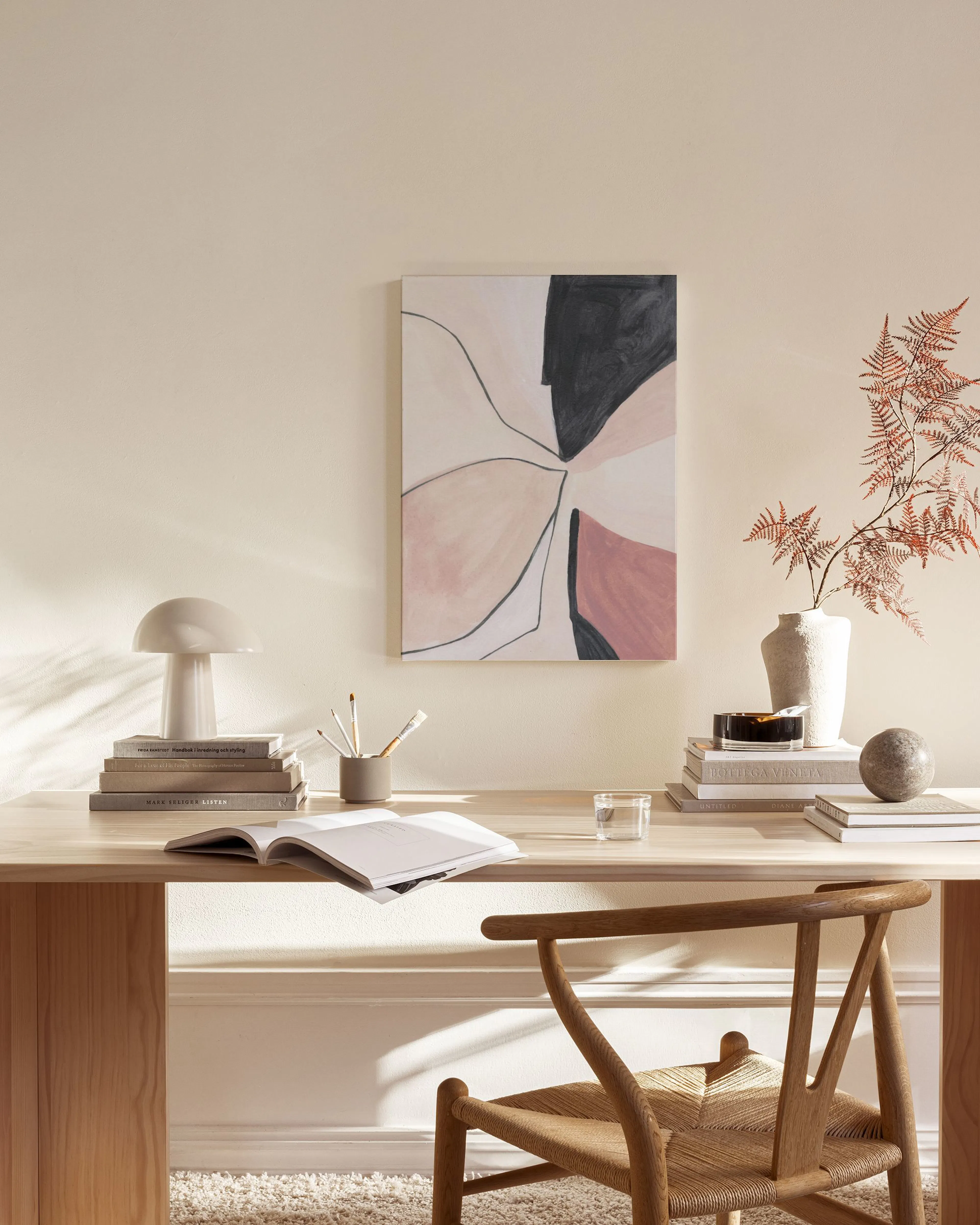 Leinwandbild mit abstrakten Formen in Schwarz, Rosa und Beige, aufgehängt in einem hellen Wohnzimmer über einem Sideboard.
