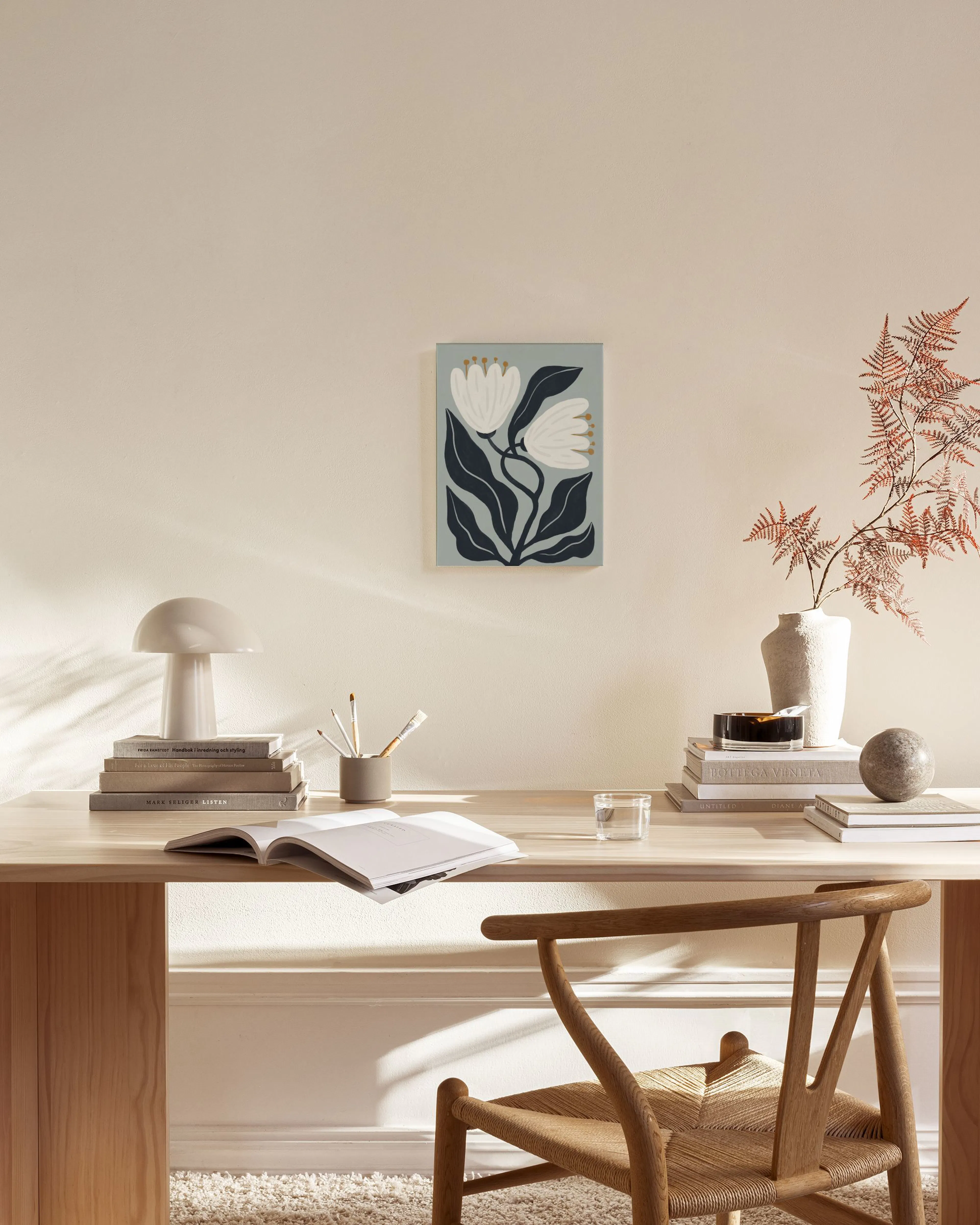 A canvas print of white flowers and dark leaves on a light blue background, hanging in a minimalist living room.