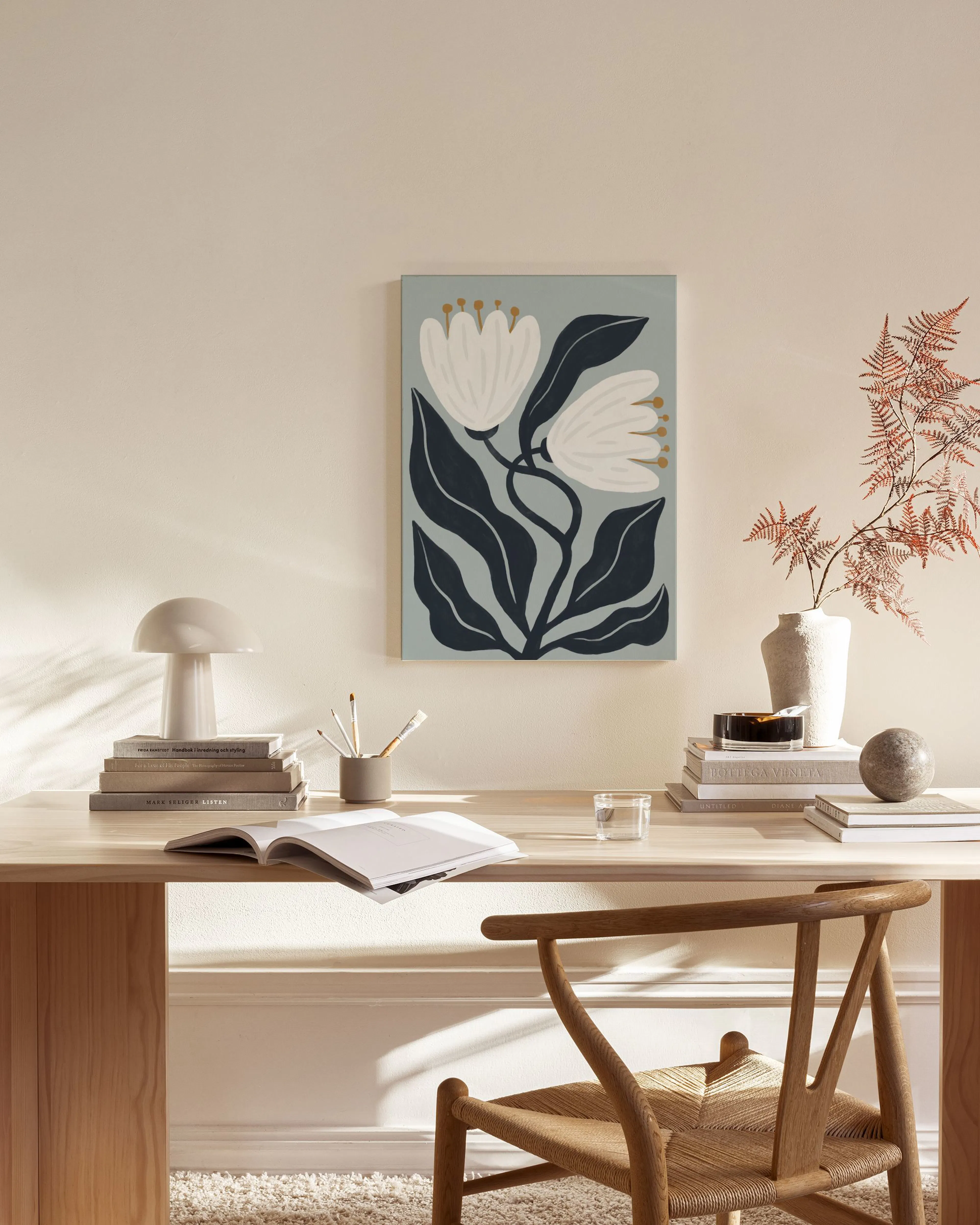 A canvas print of white flowers and dark leaves on a light blue background, hanging in a minimalist living room.