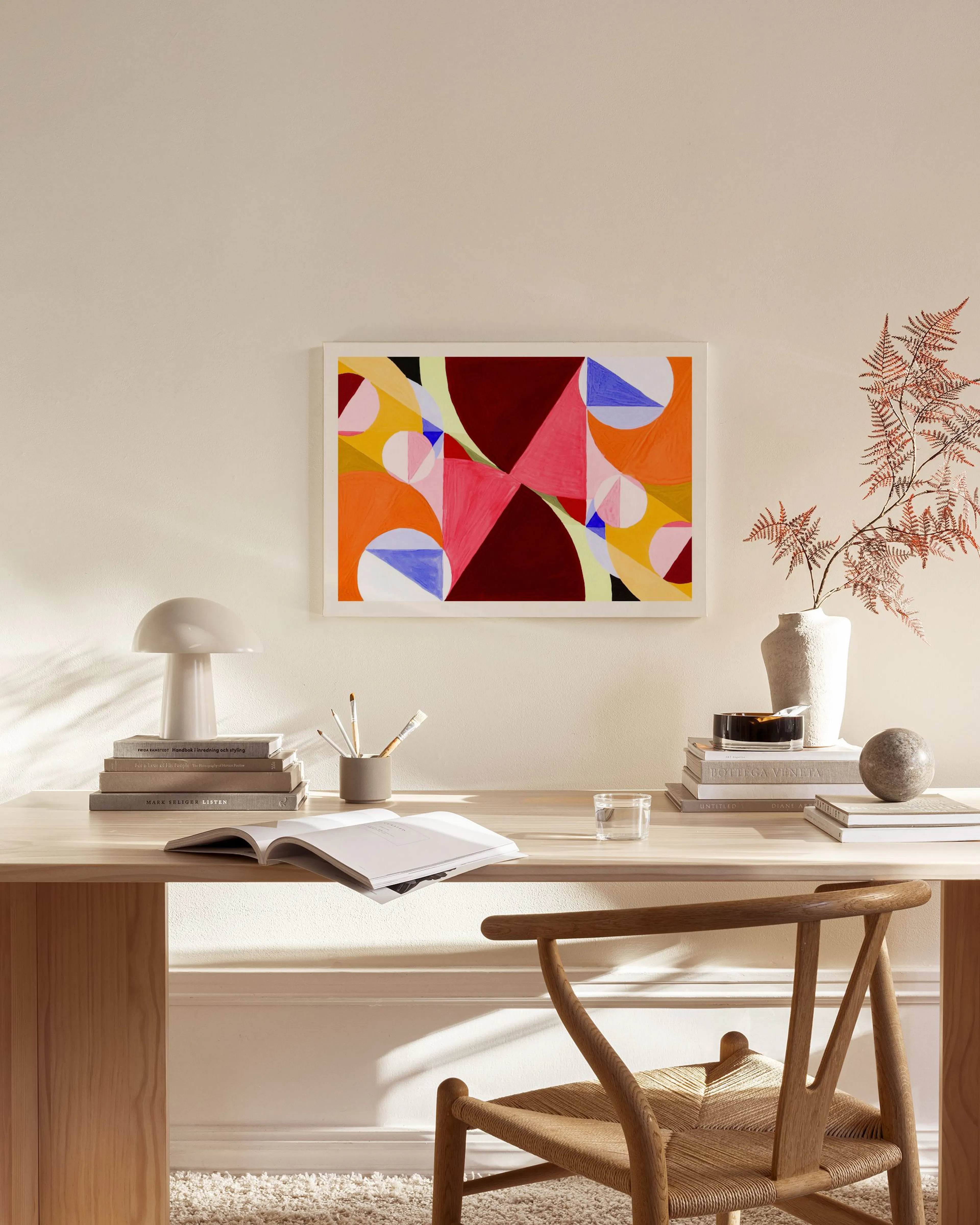 Färgglad abstrakt canvastavla med geometriska former i rött, orange och blått, hängande i ett modernt vardagsrum.