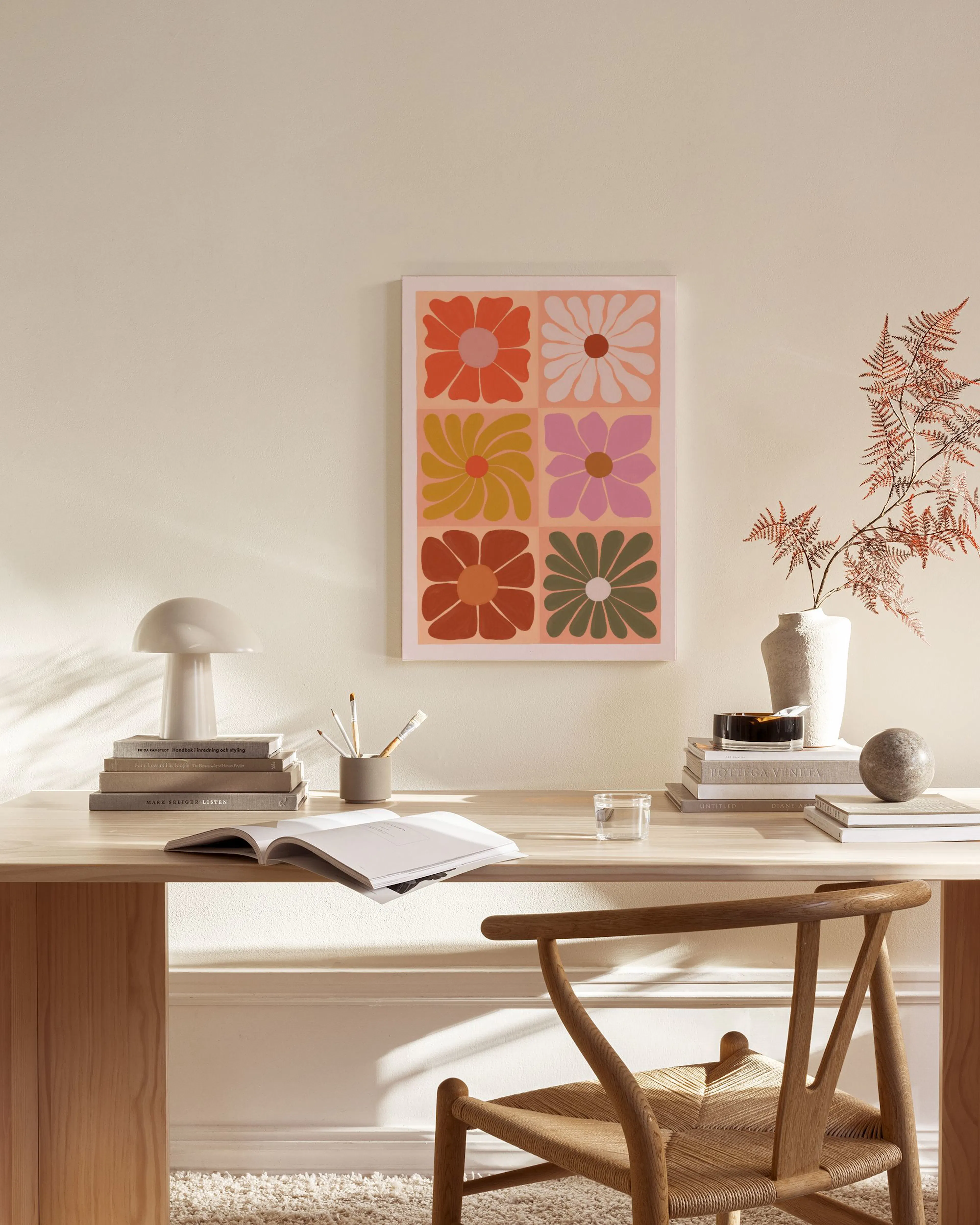 A canvas print with six colorful retro flowers on a pink background, hanging in a minimalist living room.