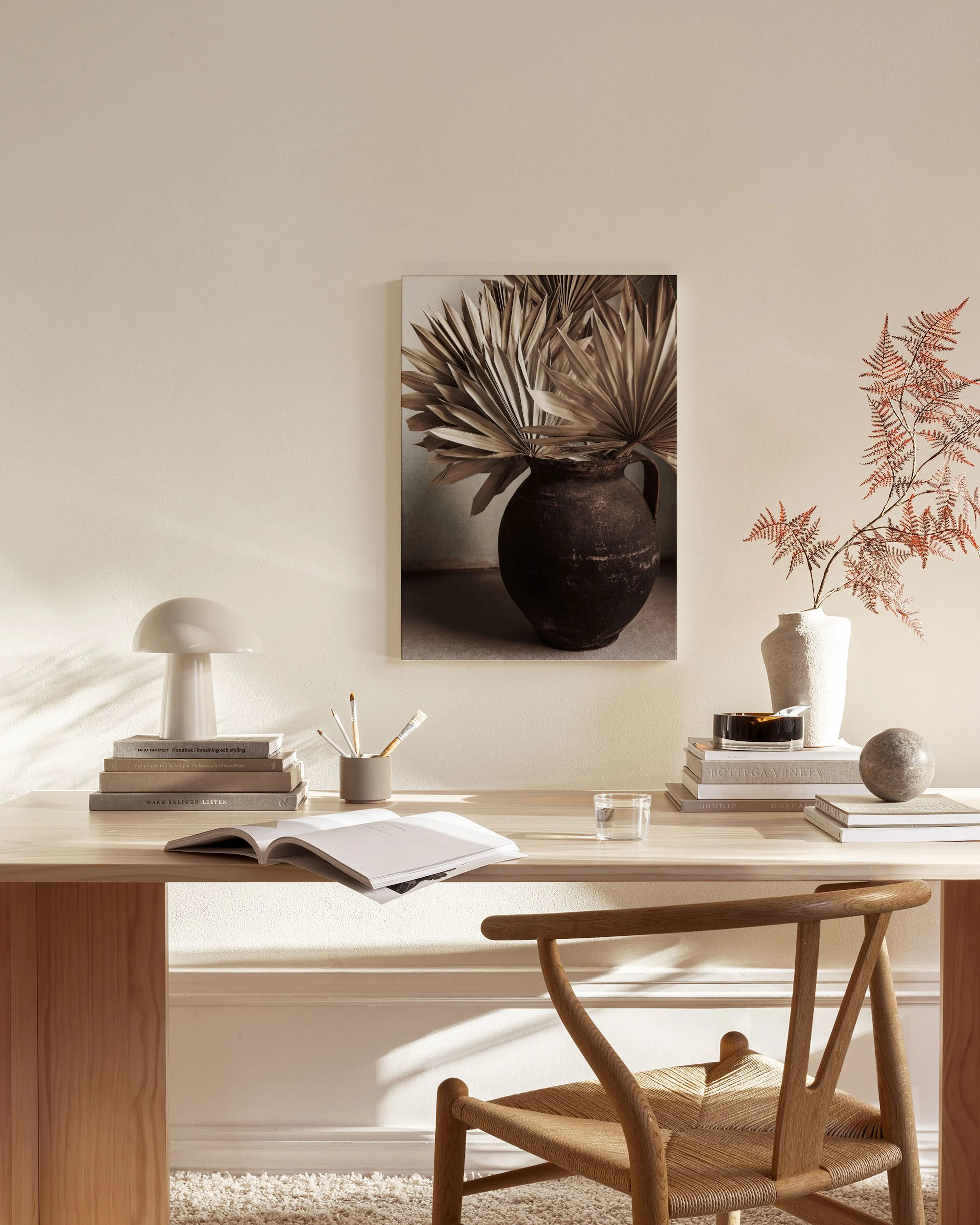 A canvas print of dried fan palm leaves in a dark textured pot, hanging above a console table in a neutral room.