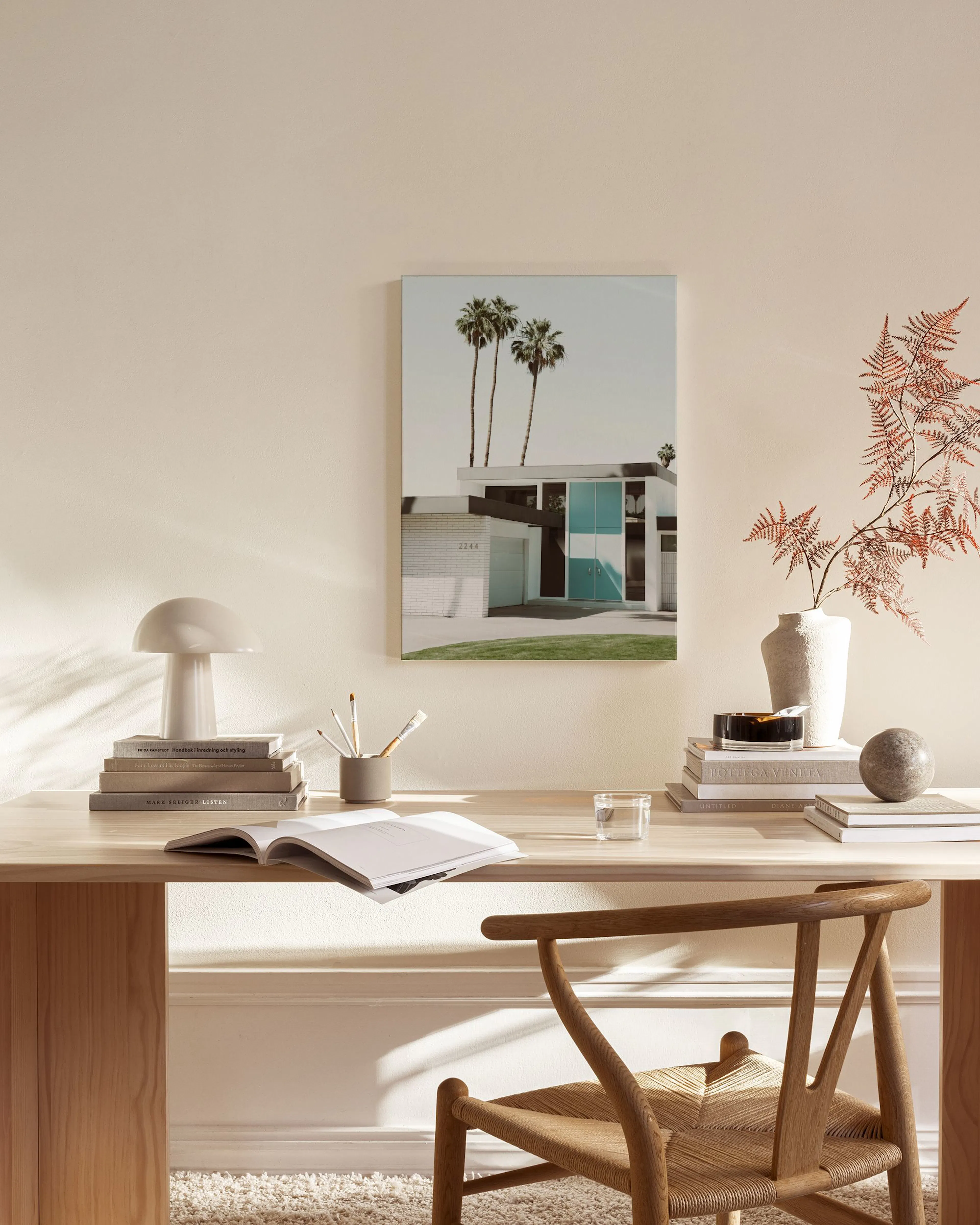 A canvas print of a modern Palm Springs house with palm trees, displayed in a light-filled living room above a wooden console.