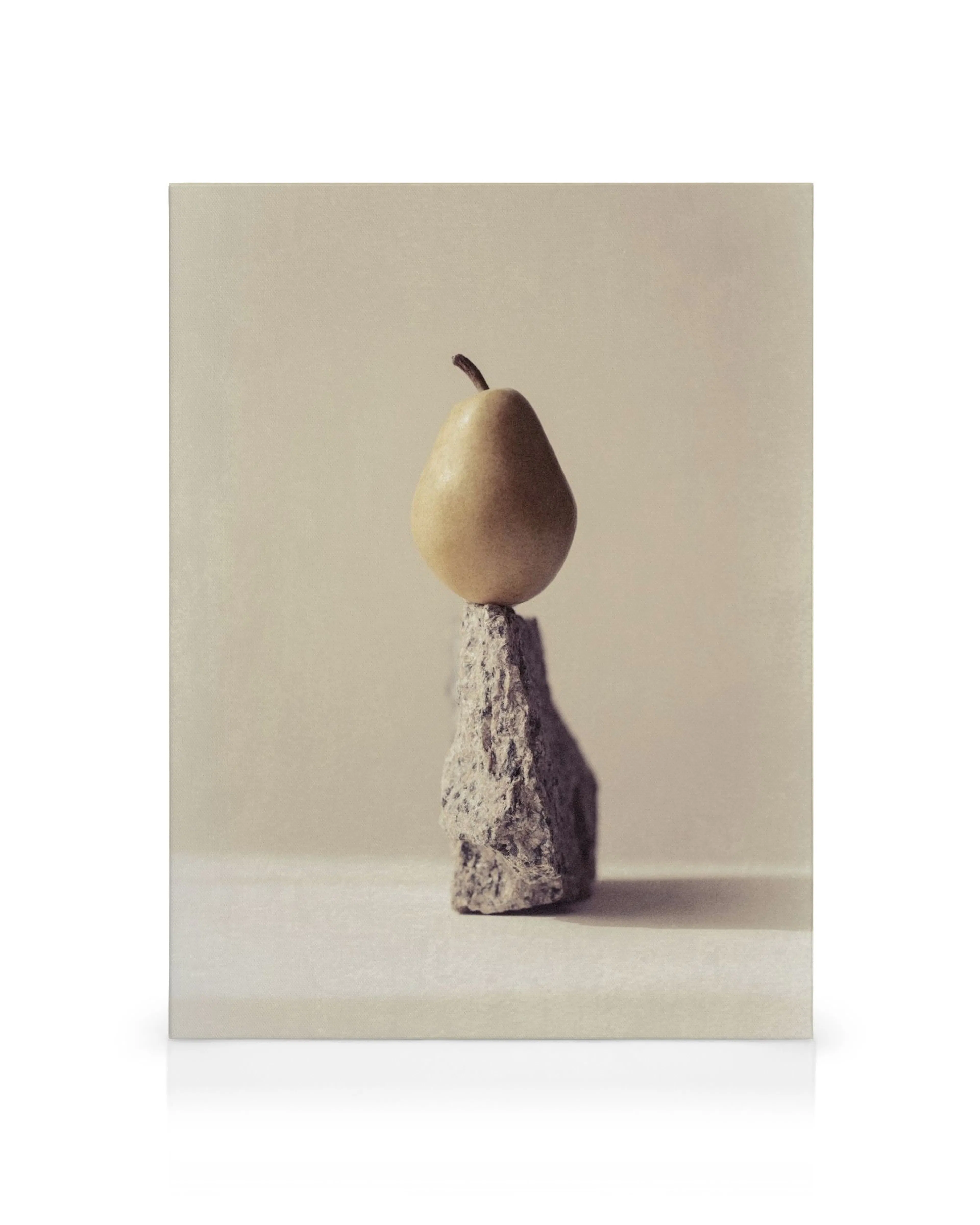 Still life of a light yellow pear balanced on a textured grey rock, against a muted beige background.