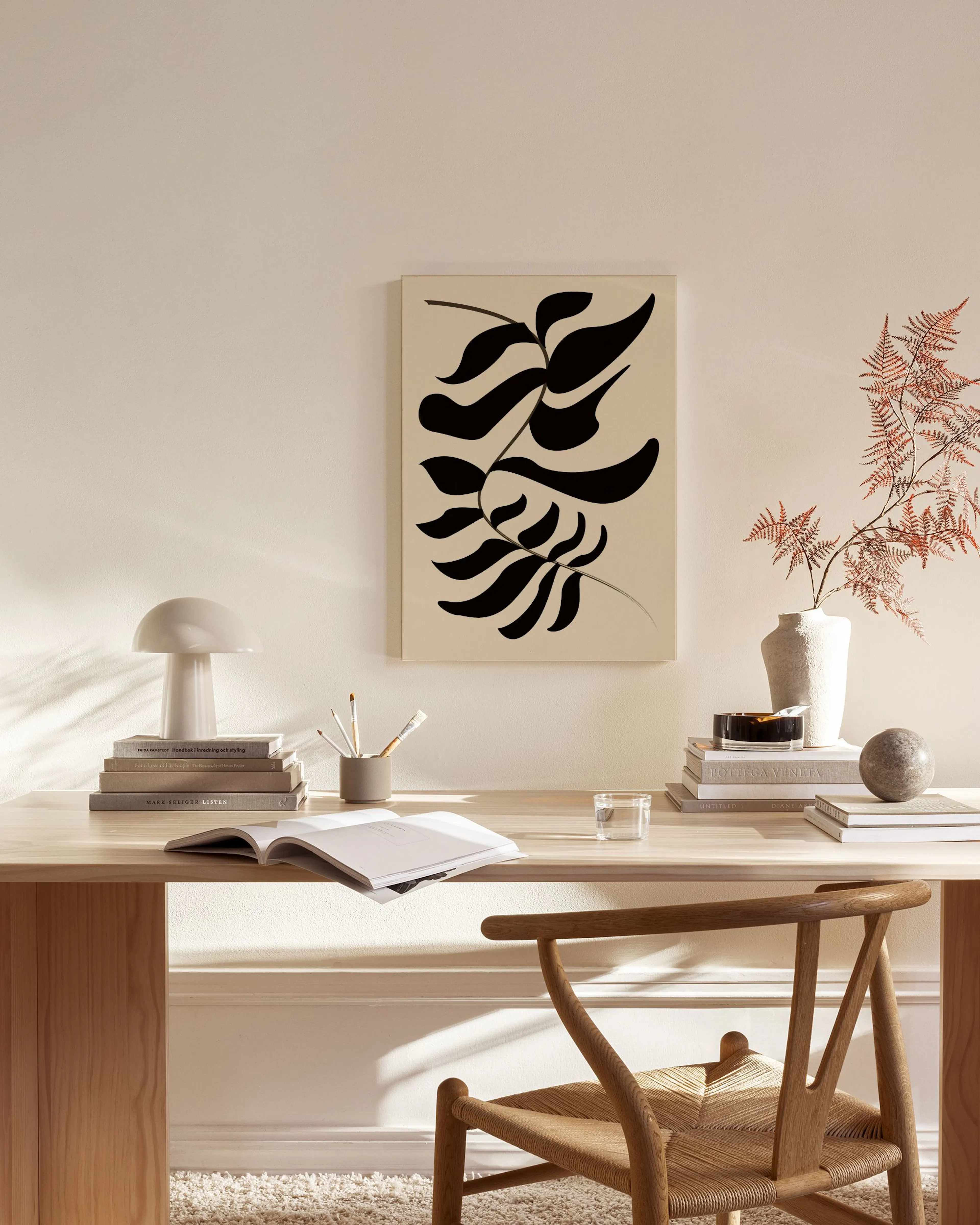 Lienzo con formas abstractas de hojas negras sobre fondo beige, colgado en una sala de estar moderna.