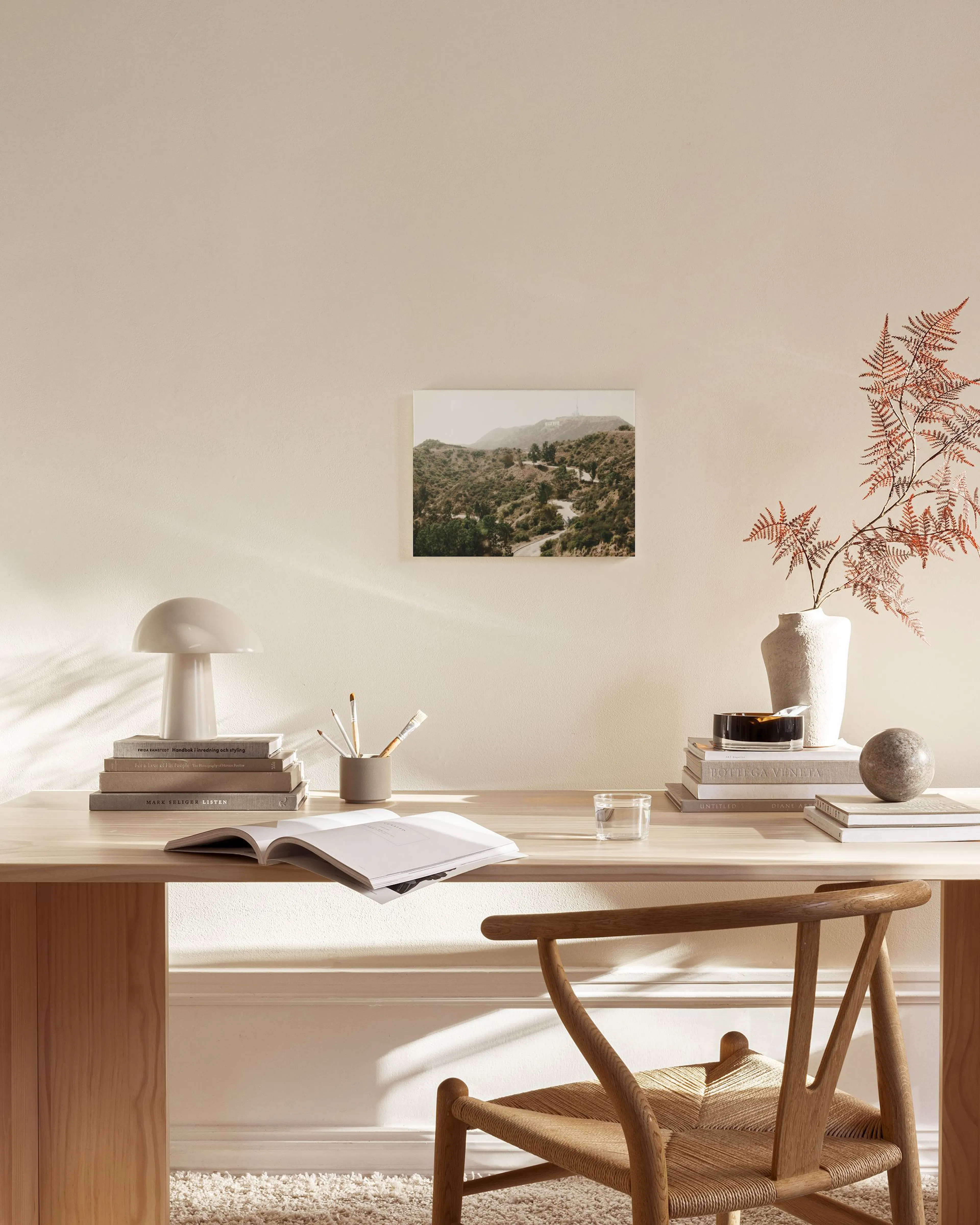A canvas print of the Hollywood sign nestled in green hills, displayed above a wooden console table in a minimalist living room.
