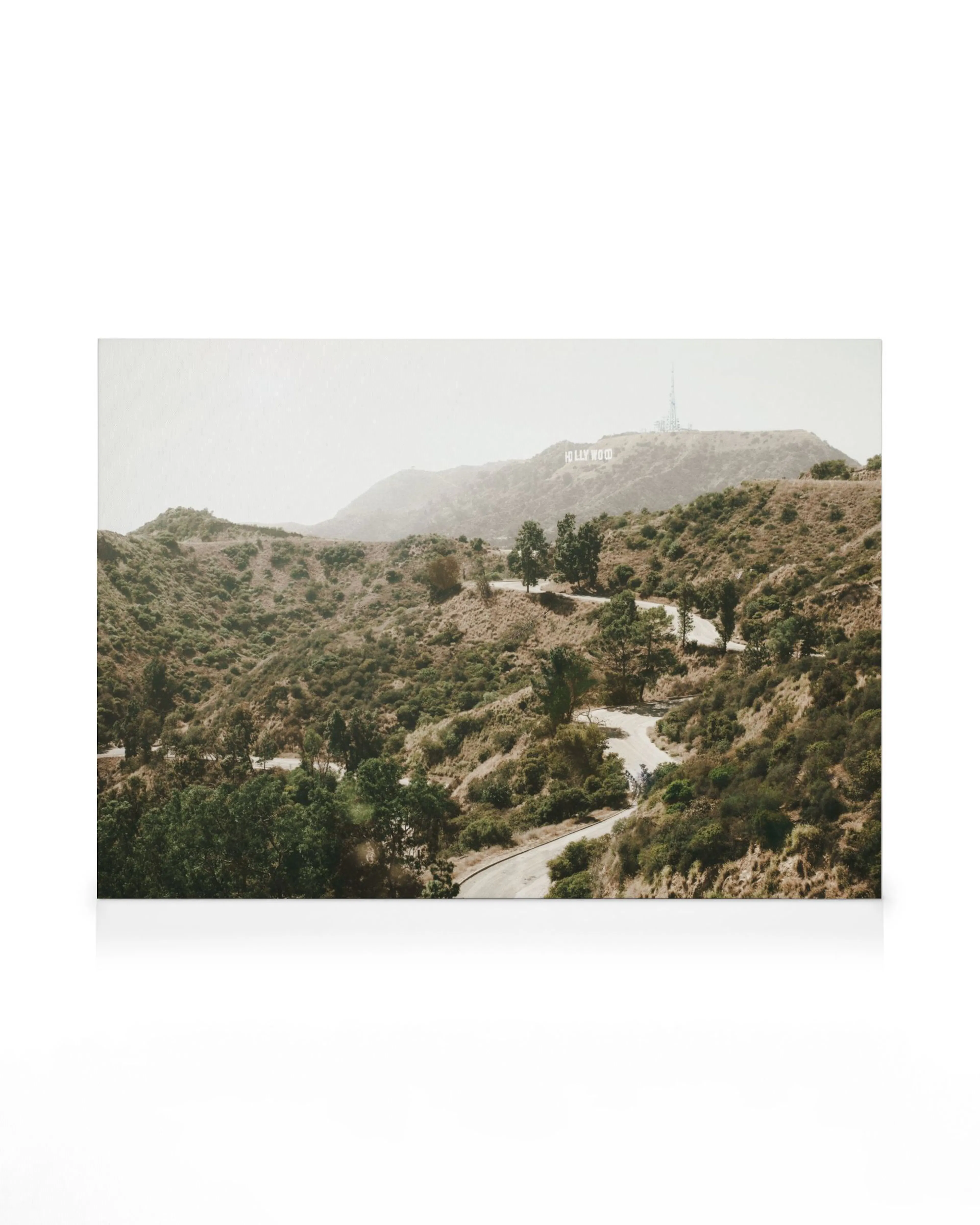Hazy photograph of a winding road through rolling green hills with white letters on a far-off hilltop.