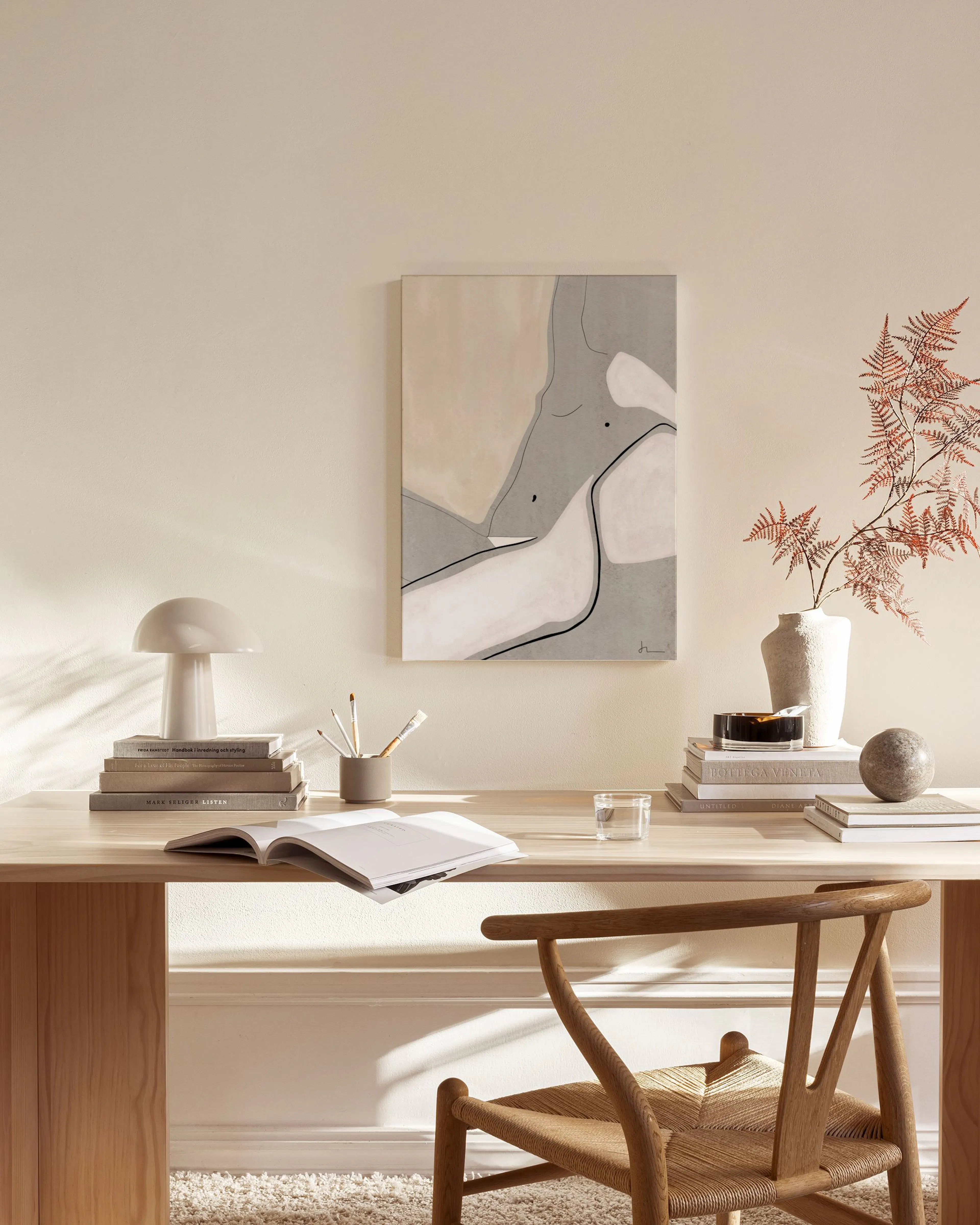 A canvas print with beige, grey, and white organic shapes and black flowing lines, hanging in a minimalist living room.