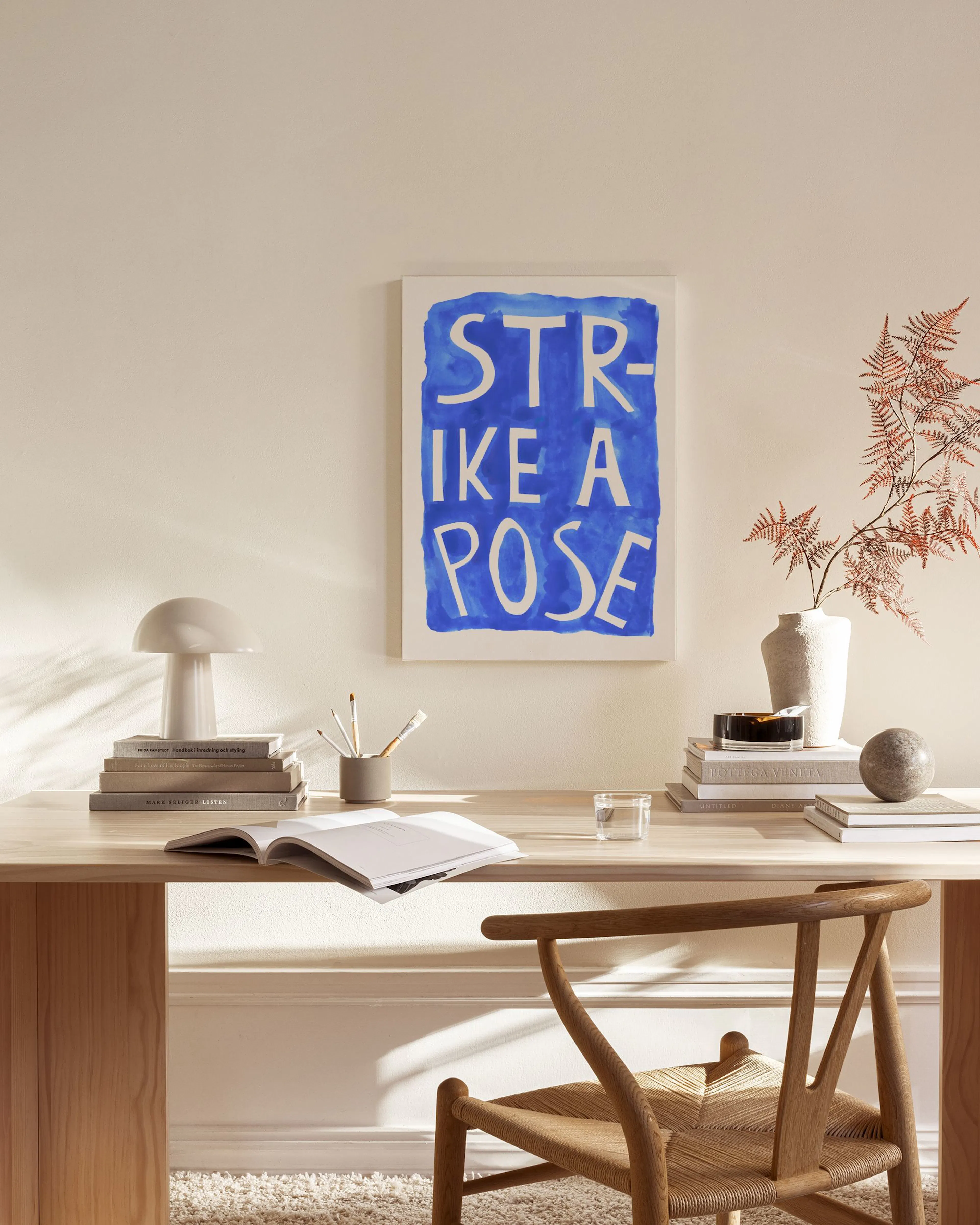 Toile Strike a Pose bleue et blanche, accrochée dans un salon moderne avec fauteuil en bois clair et table basse.