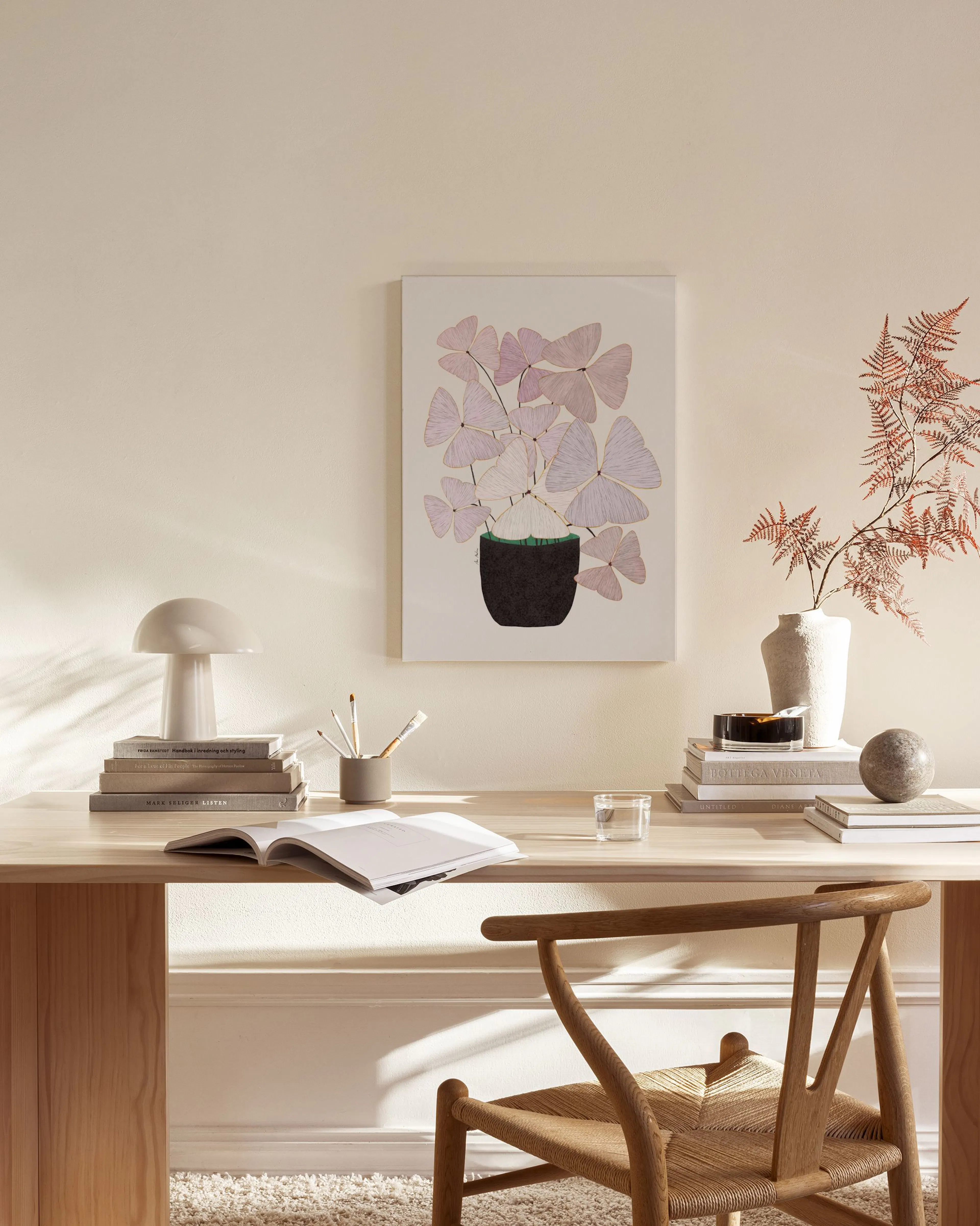 Een canvas met een plant van roze vlindervormige bladeren in een donkere pot, hangend boven een houten dressoir in een lichte wo