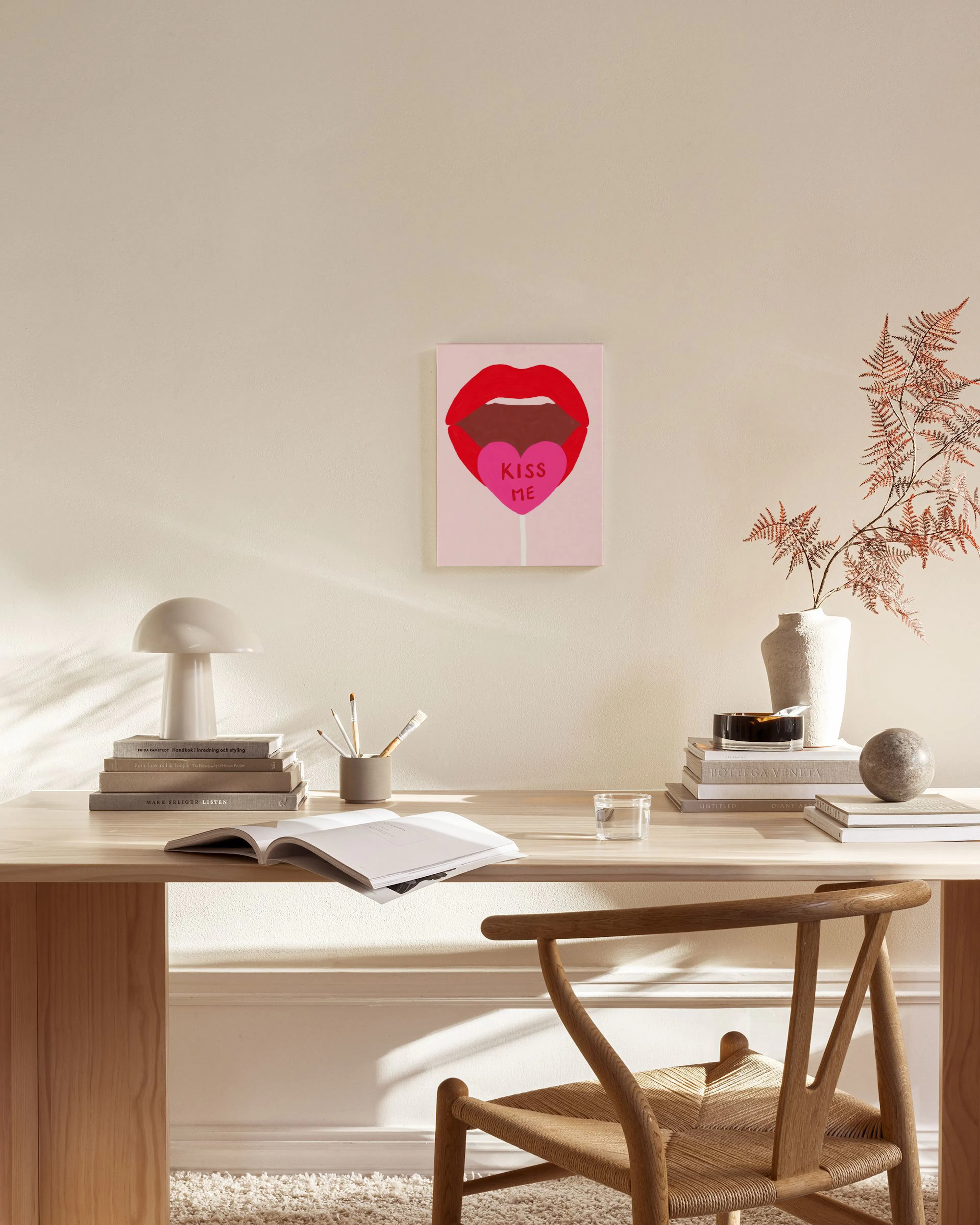 Canvastavla med röda läppar som håller en rosa klubba med KISS ME, hänger i ett ljust vardagsrum.