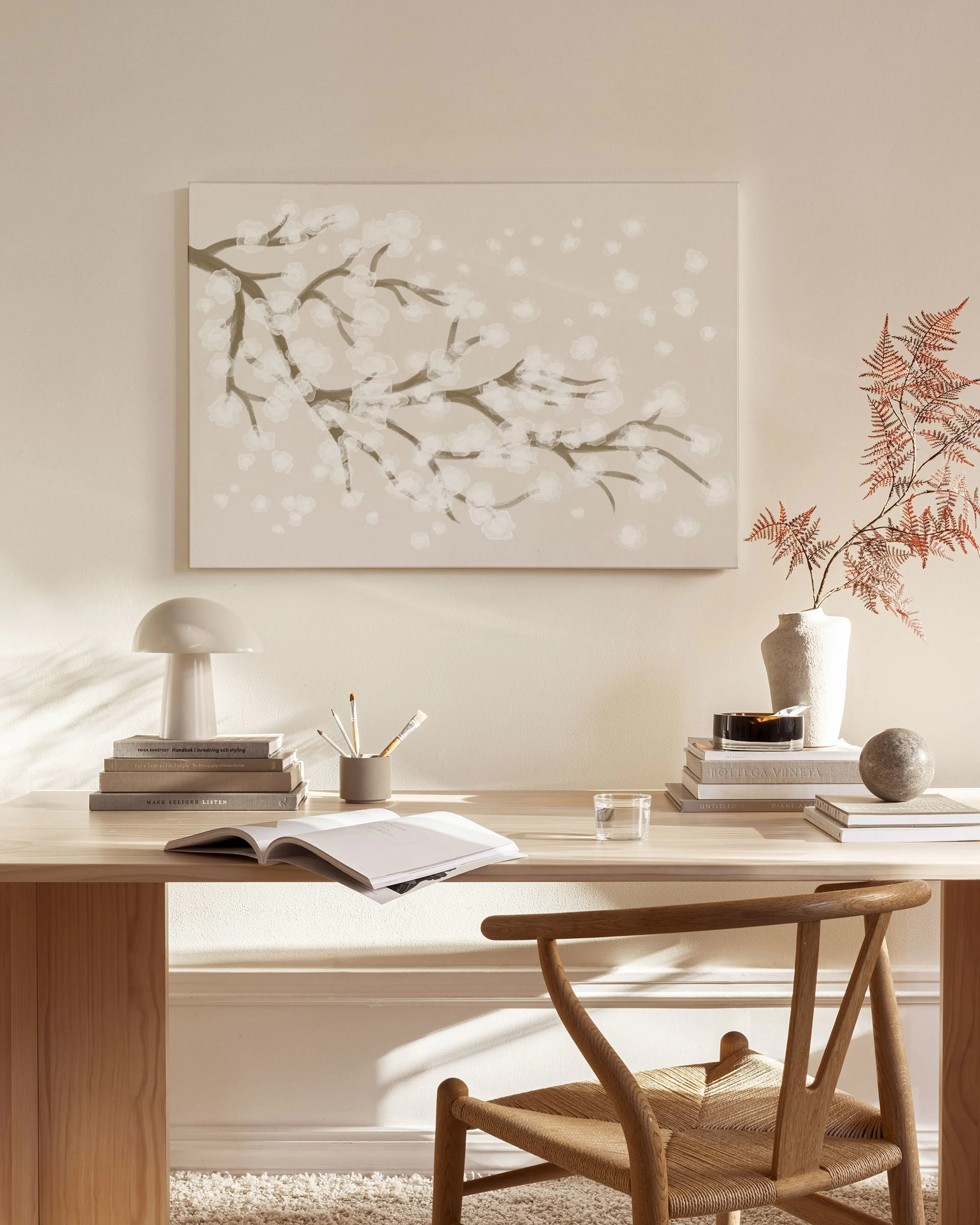 A canvas print of white cherry blossoms on a light brown background, hanging above a wooden console table in a minimalist living