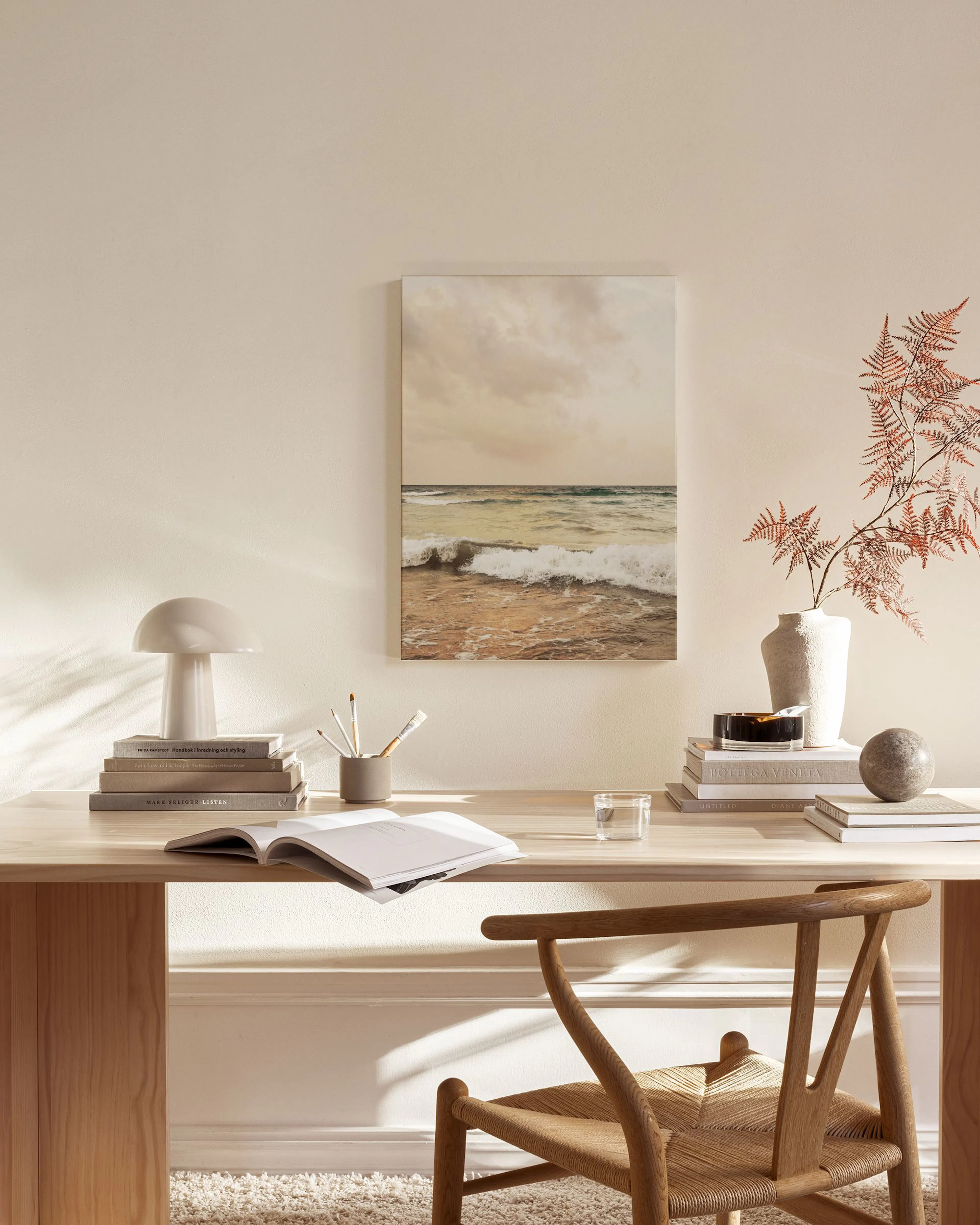 A canvas print of ocean waves under a cloudy sky, hanging above a wooden console in a minimalist living room.