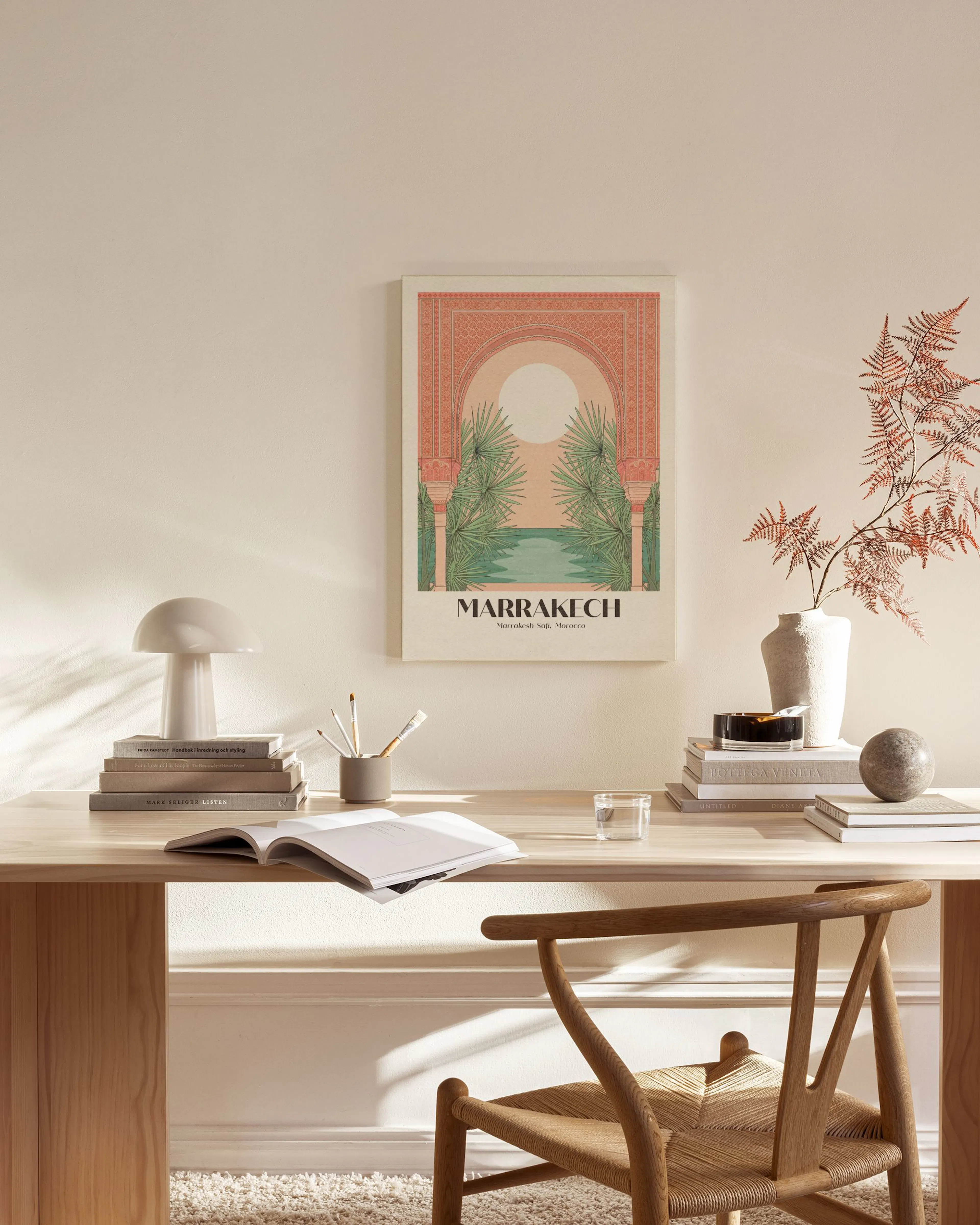 A Marrakech travel poster with a coral archway, green palm trees, and a pool, displayed in a modern living room.