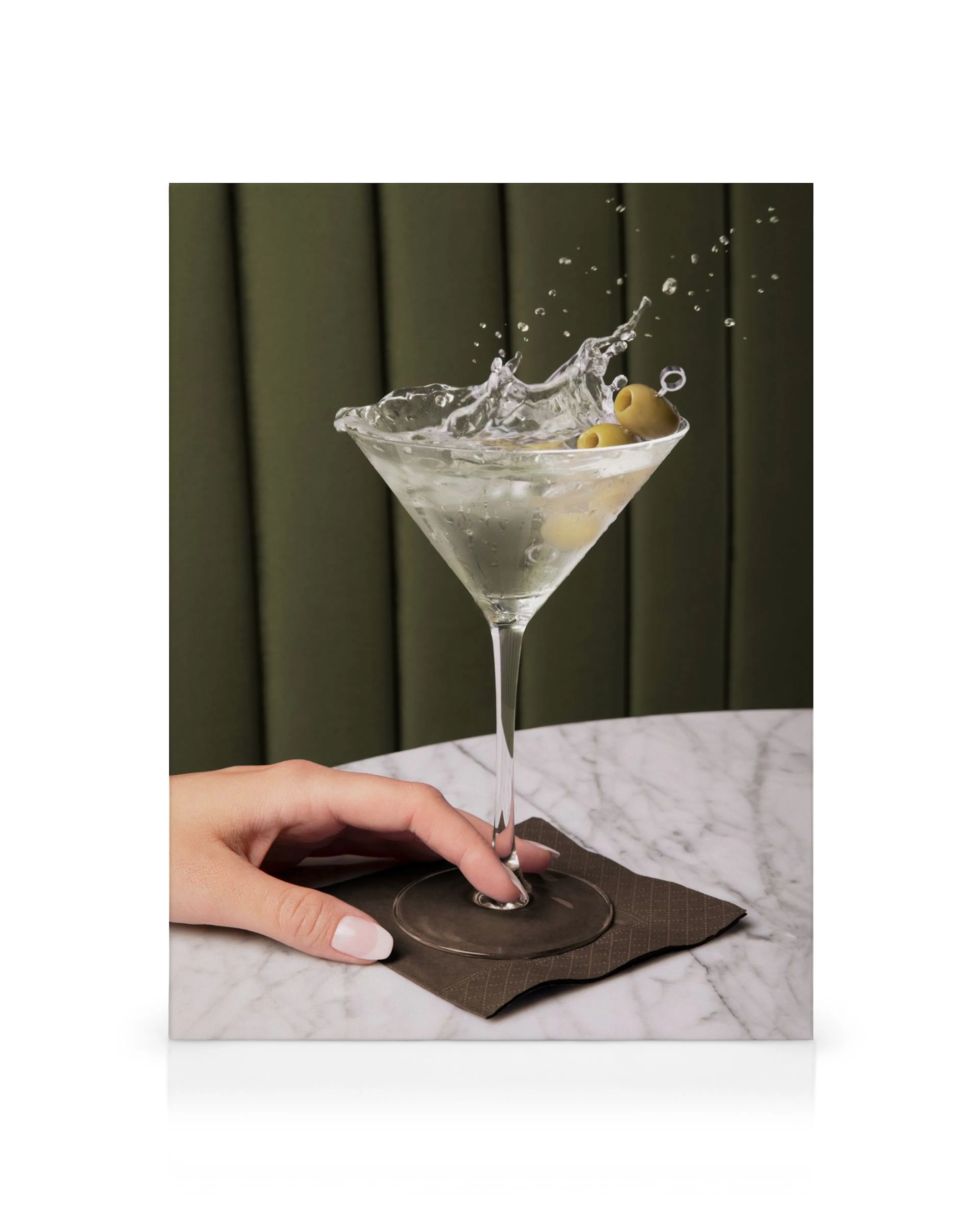 Martini im Glas mit Oliven, Spritzwasser, Hand auf Marmortisch, grüner Hintergrund