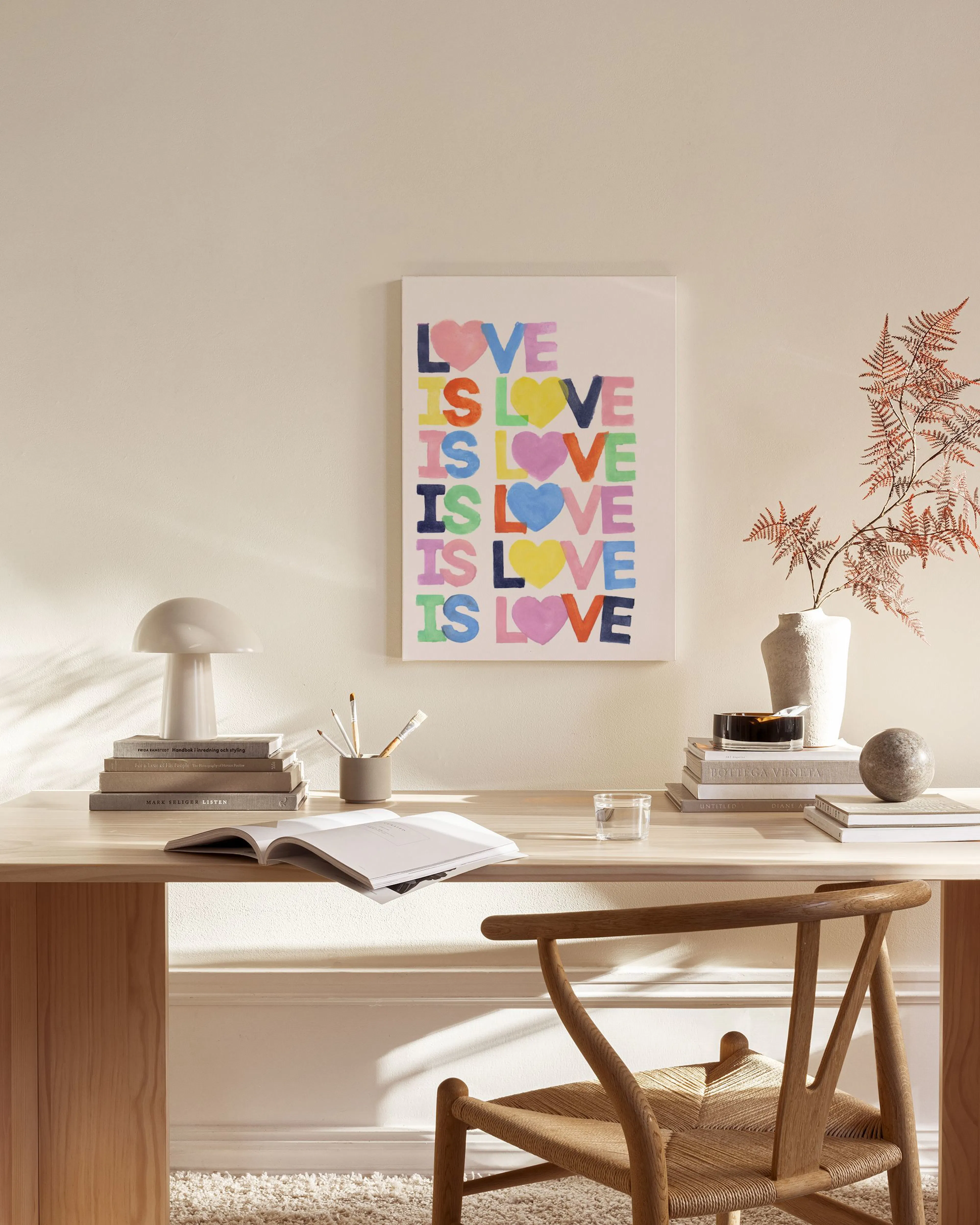 Buntes Leinwandbild mit LOVE IS LOVE“ in Herz-Buchstaben, hängt in einem modernen Wohnzimmer über einem Sideboard.