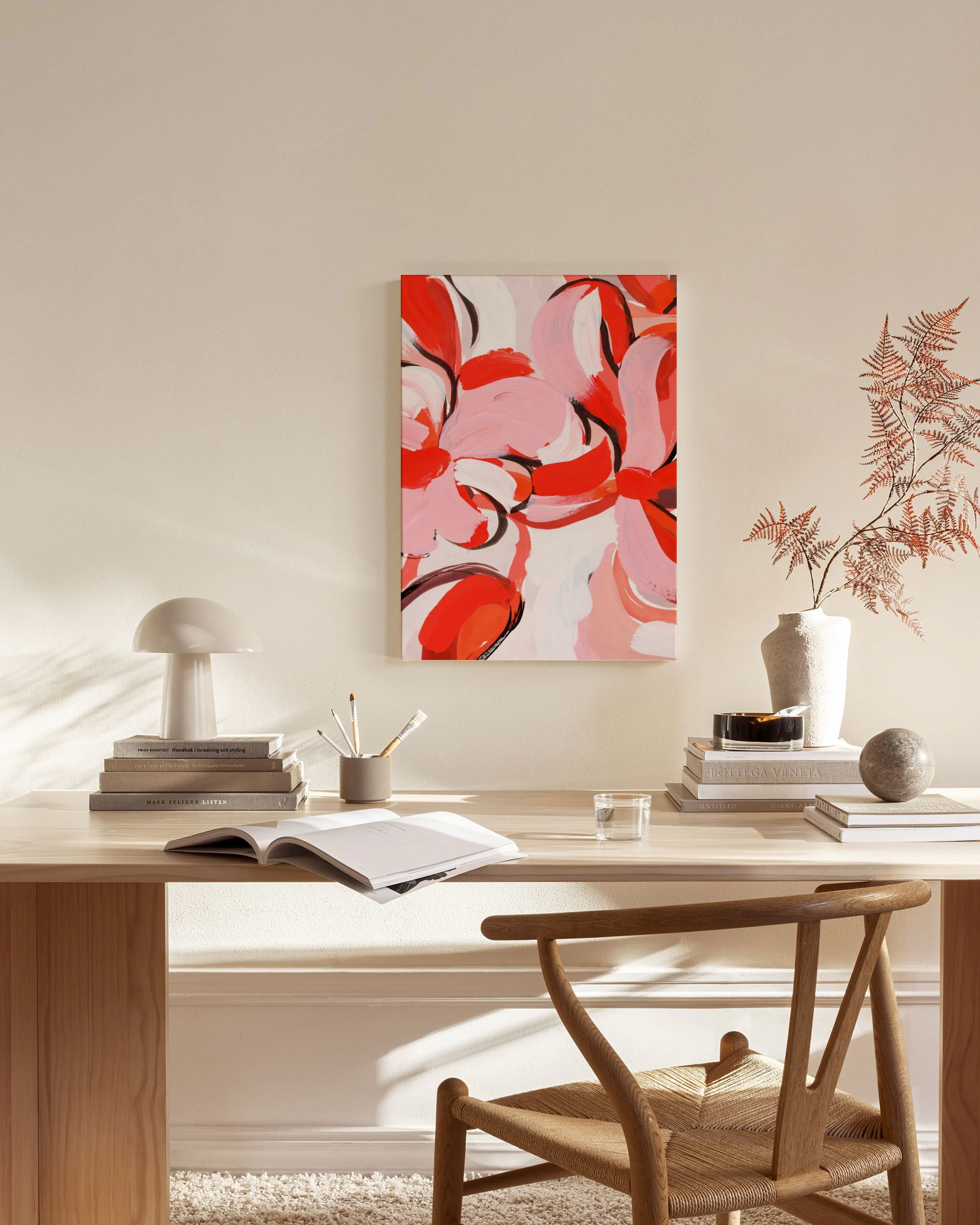 Stampa su tela astratta con forme floreali rosse, rosa e nere su sfondo bianco, appesa in un soggiorno moderno.