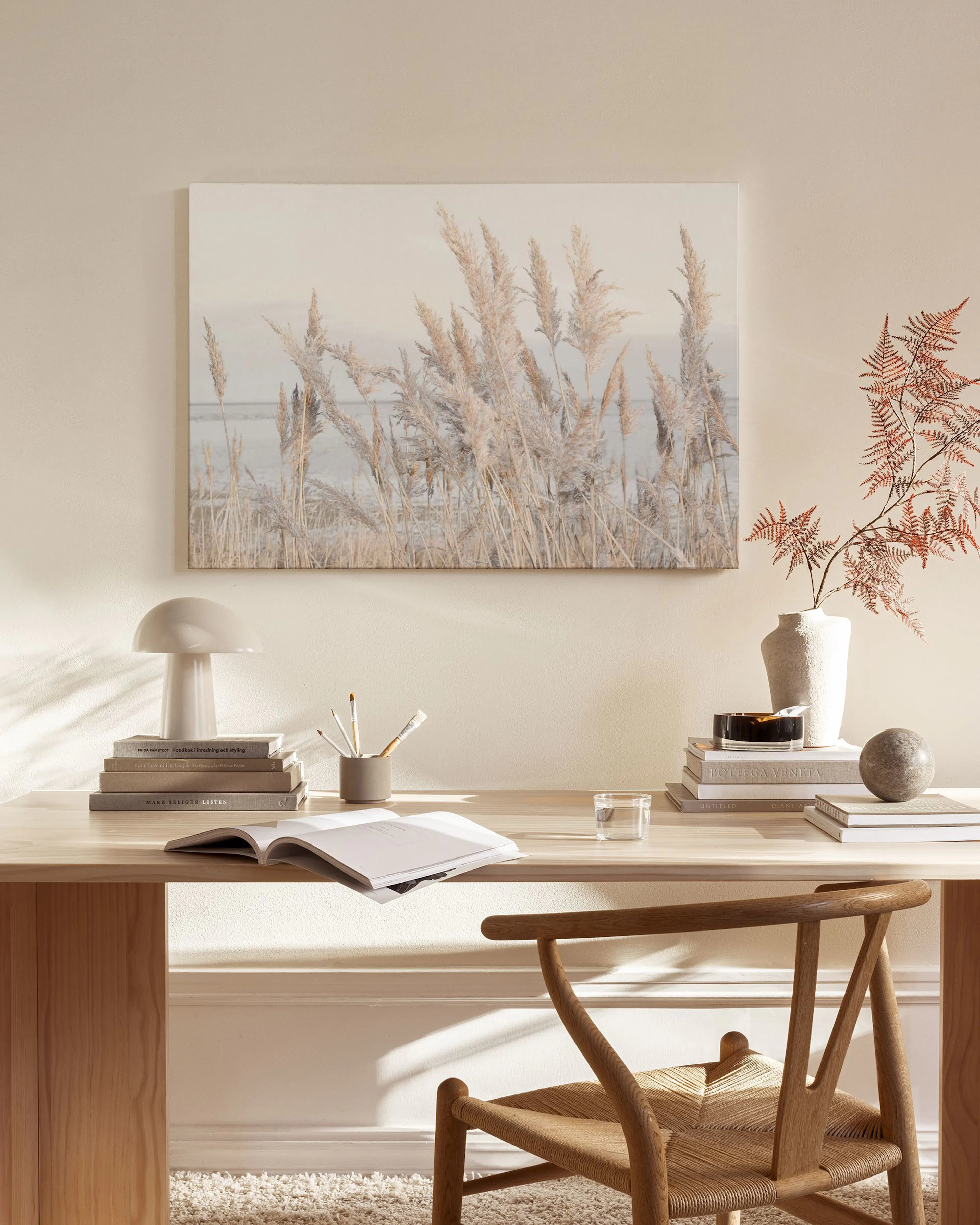 Lienzo de plantas de pampa de tonos neutros sobre un lago, colgado en una sala de estar moderna con muebles de madera.