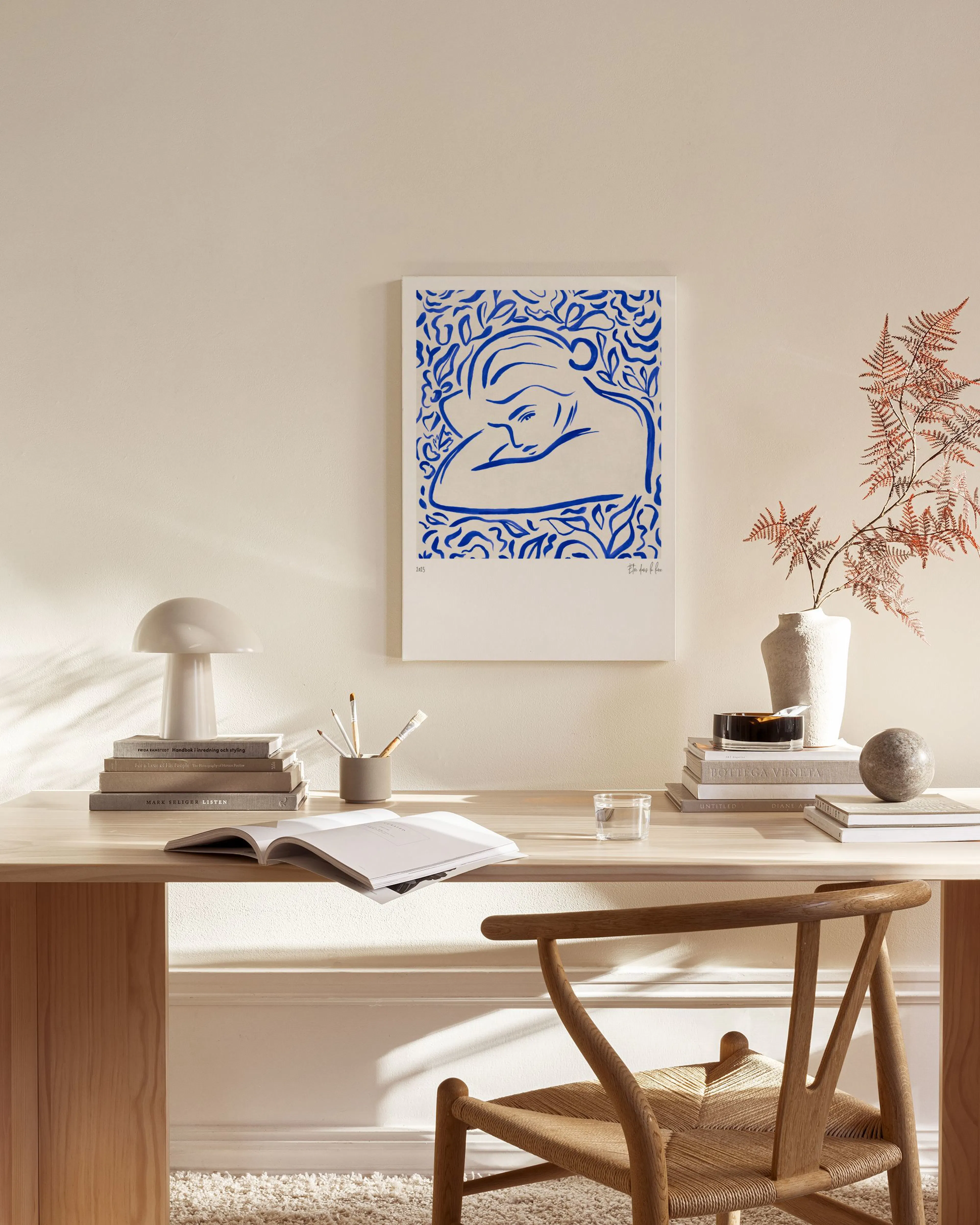 Leinwandbild einer ruhenden Frau in Blau auf Weiß, umgeben von Blättern, über einem Sideboard im Wohnzimmer.