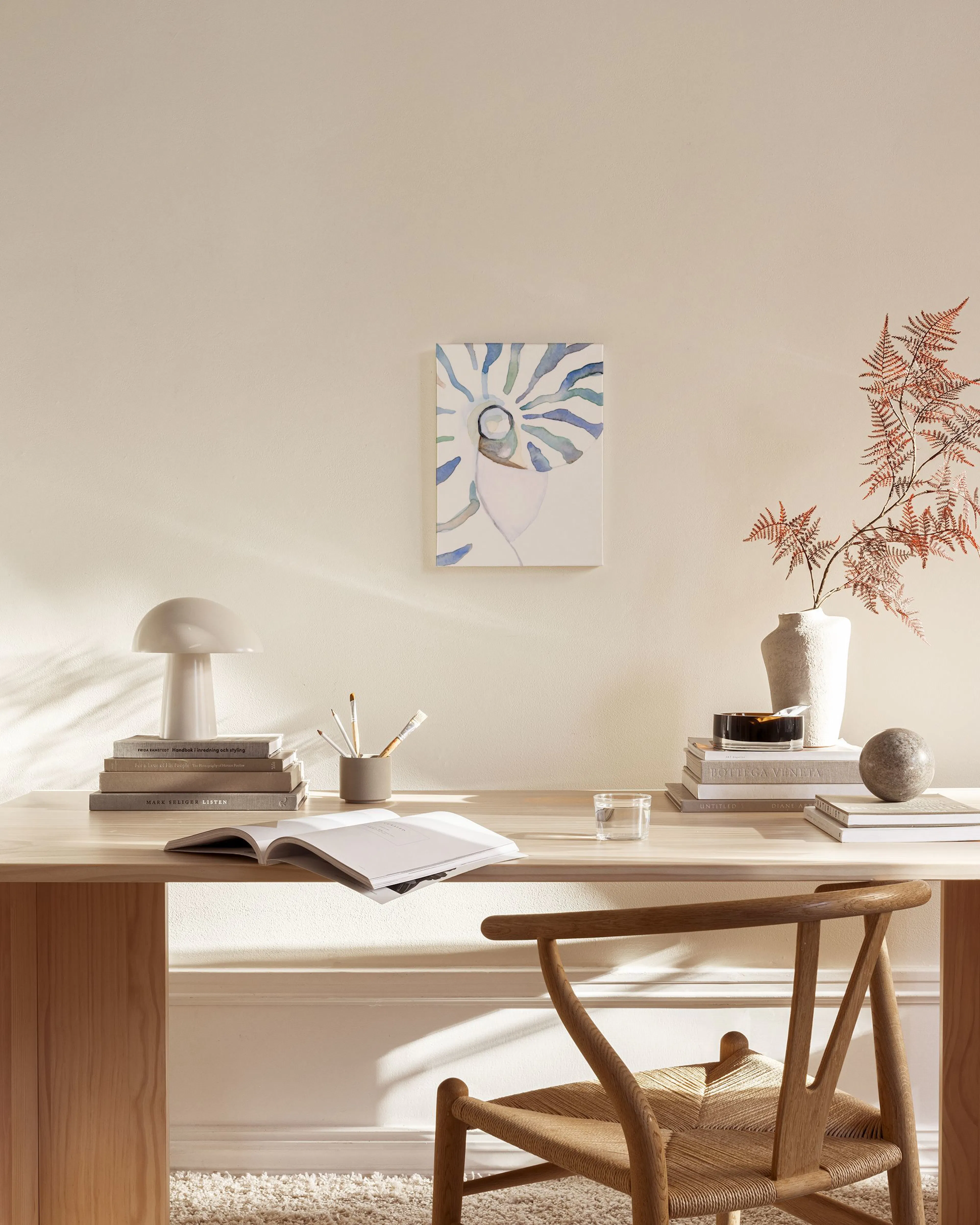 Water-colored nautilus shell canvas print with blue and green hues, hanging in a minimalist living room.