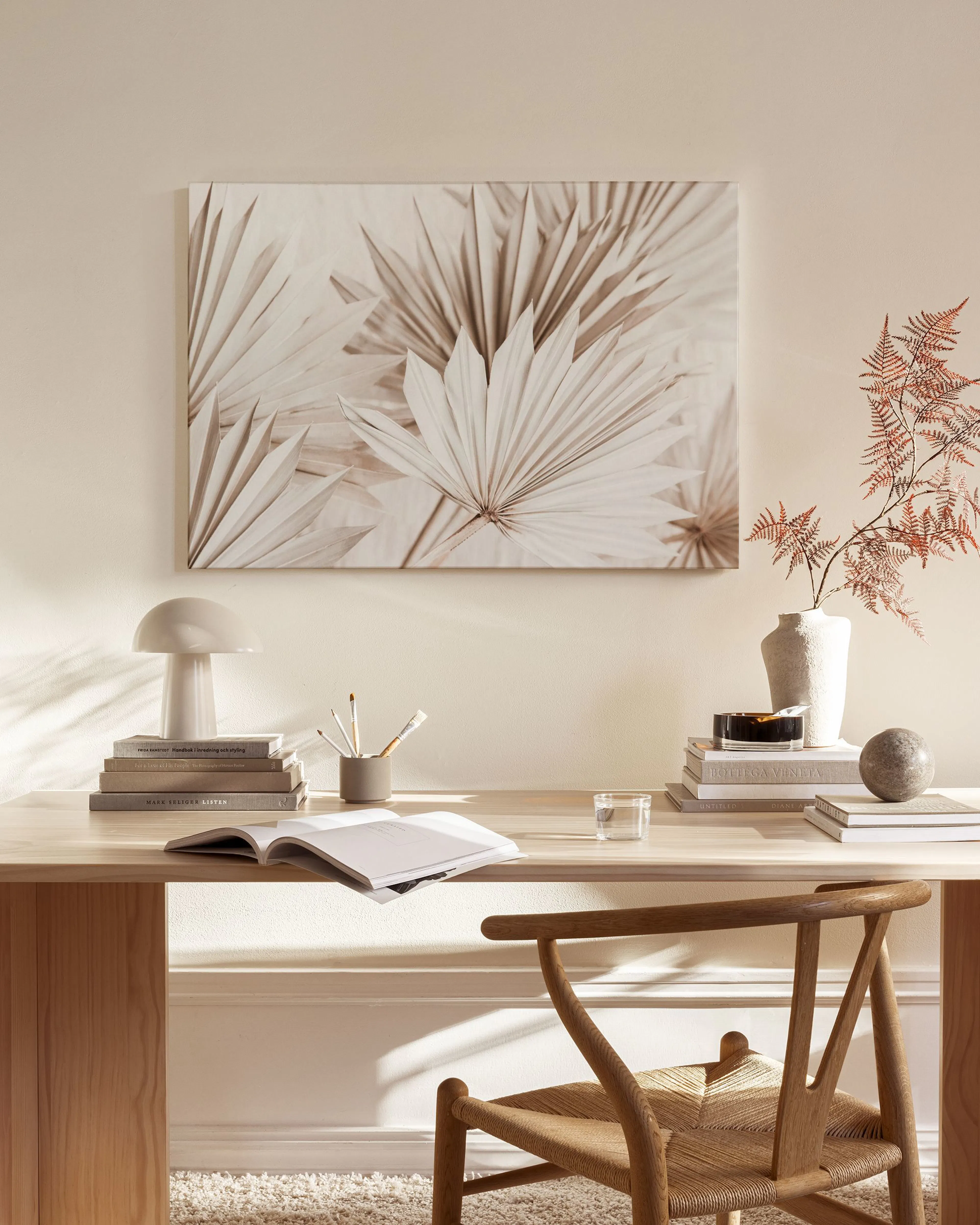 A canvas print of dried fan palm leaves in beige and white tones, hanging above a console table in a minimalist living room.