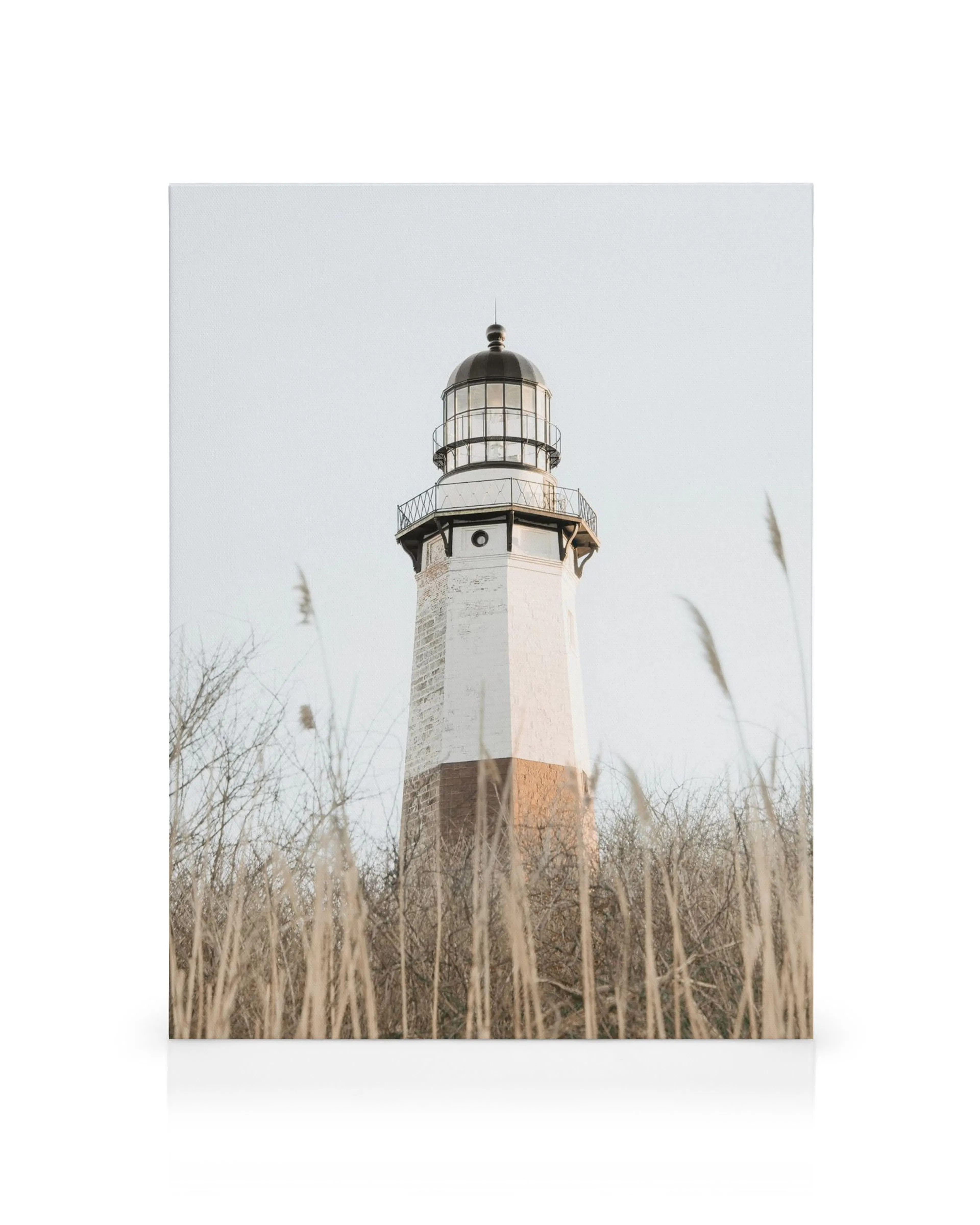 Hoge vuurtoren met zwart, wit, bruin en beige tinten, omringd door droog gras tegen een lichtblauwe lucht.