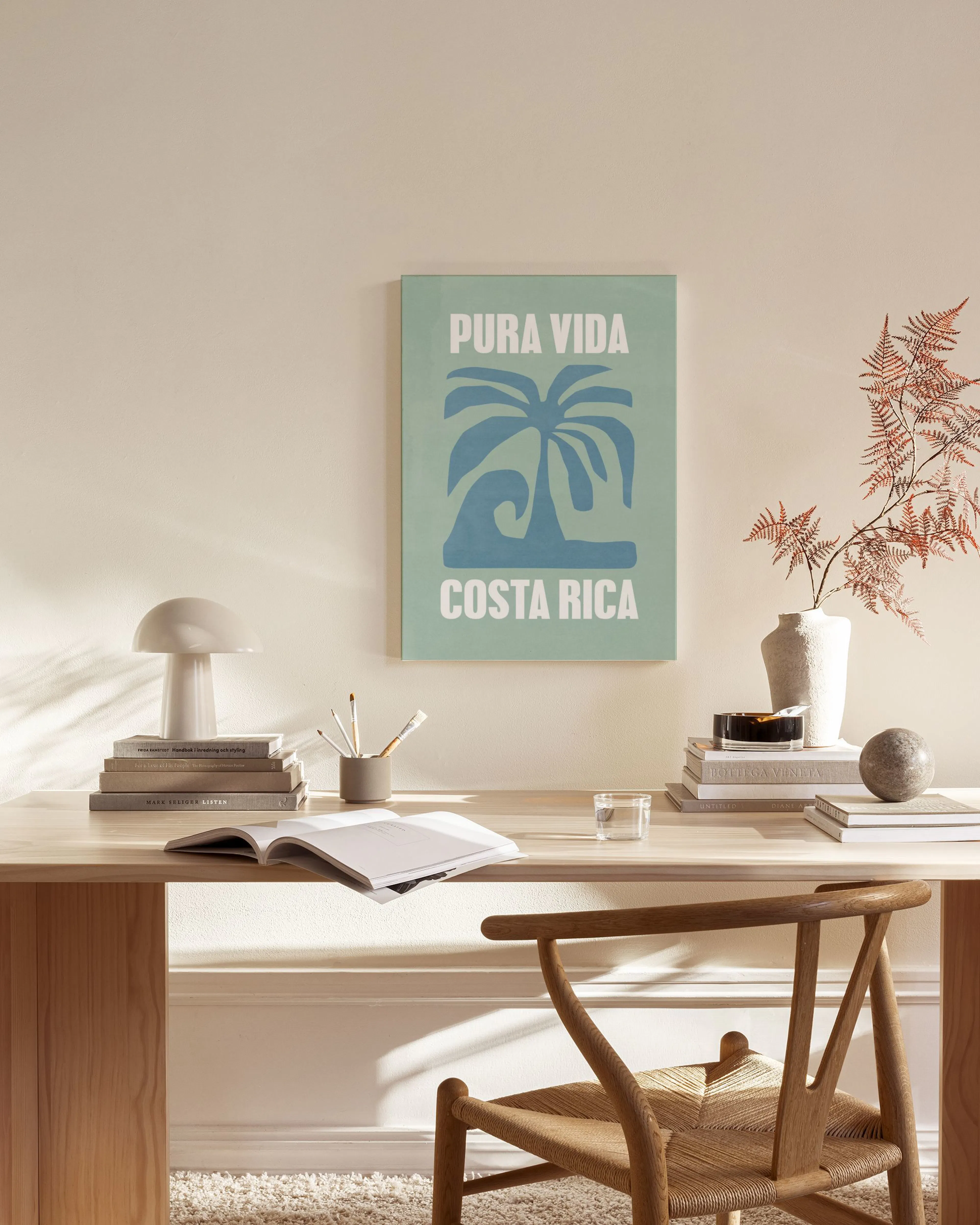 Canvastavla med texten Pura Vida Costa Rica och en stiliserad palmträd/våg i beige och blått, hängande i ett ljust vardagsrum.
