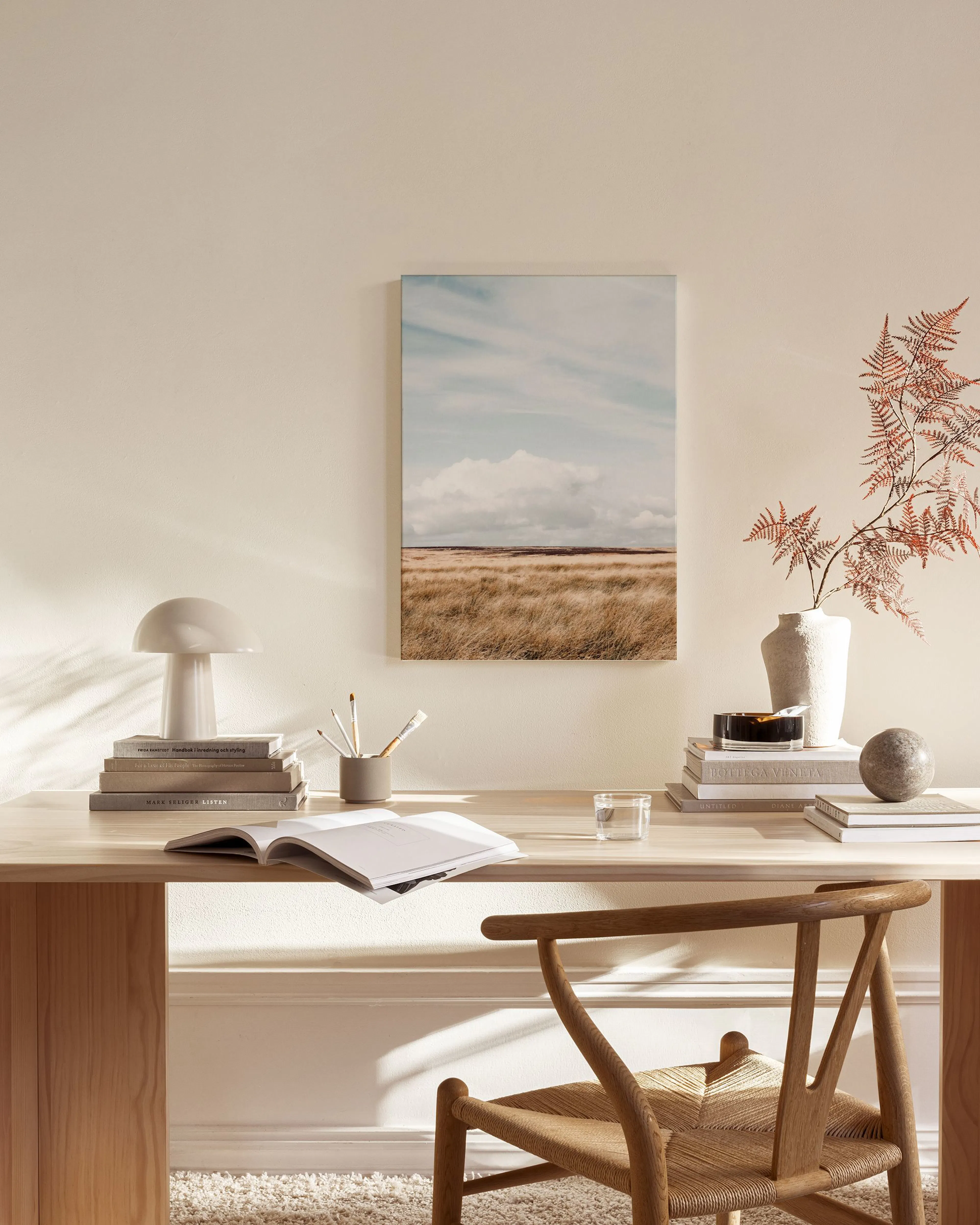 Canvas met een landschap van bruine velden onder een bewolkte blauwe lucht, hangend in een lichte woonkamer.