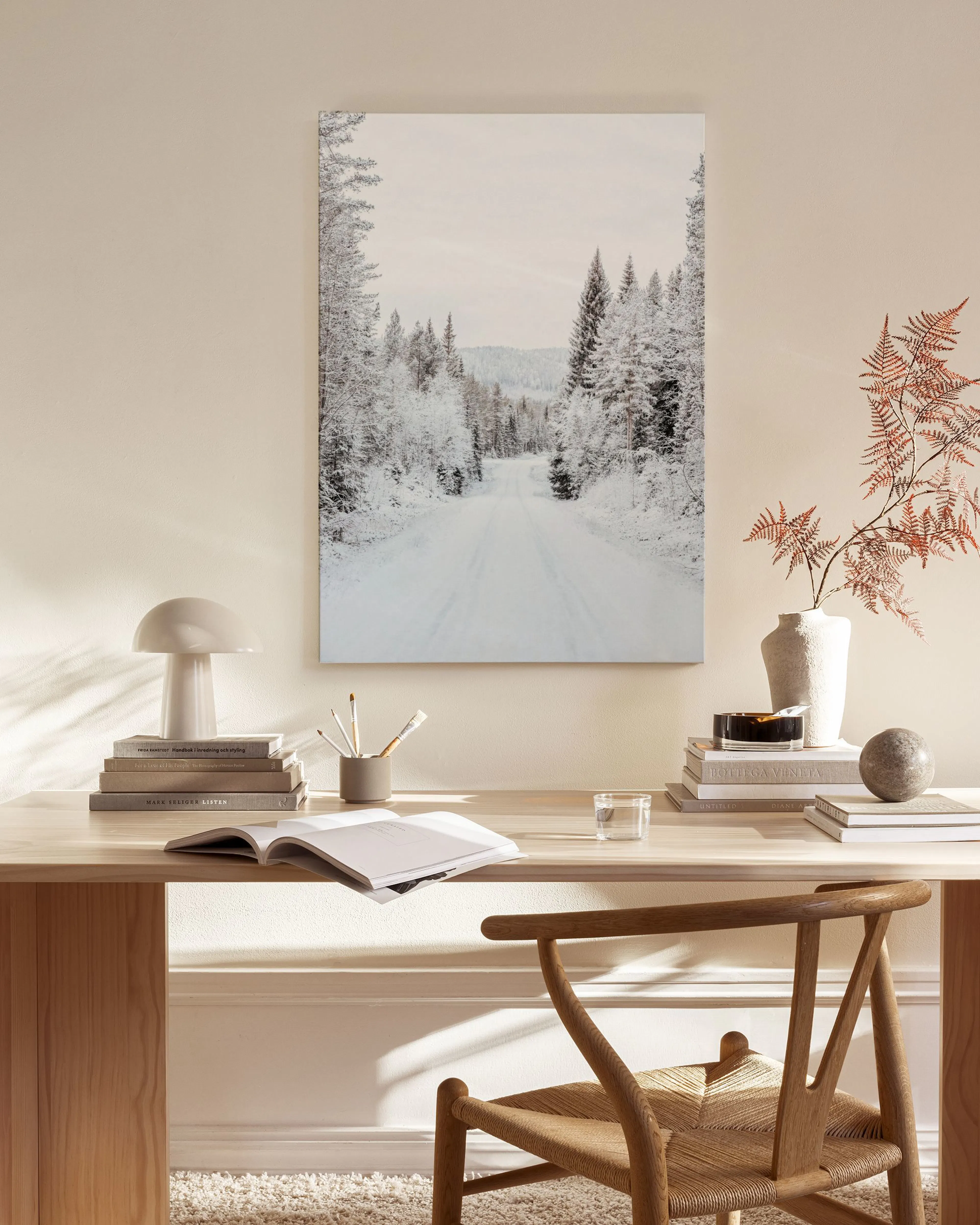 Canvastavla med en snötäckt väg som leder genom ett vinterlandskap med träd, upphängd i ett ljust vardagsrum.