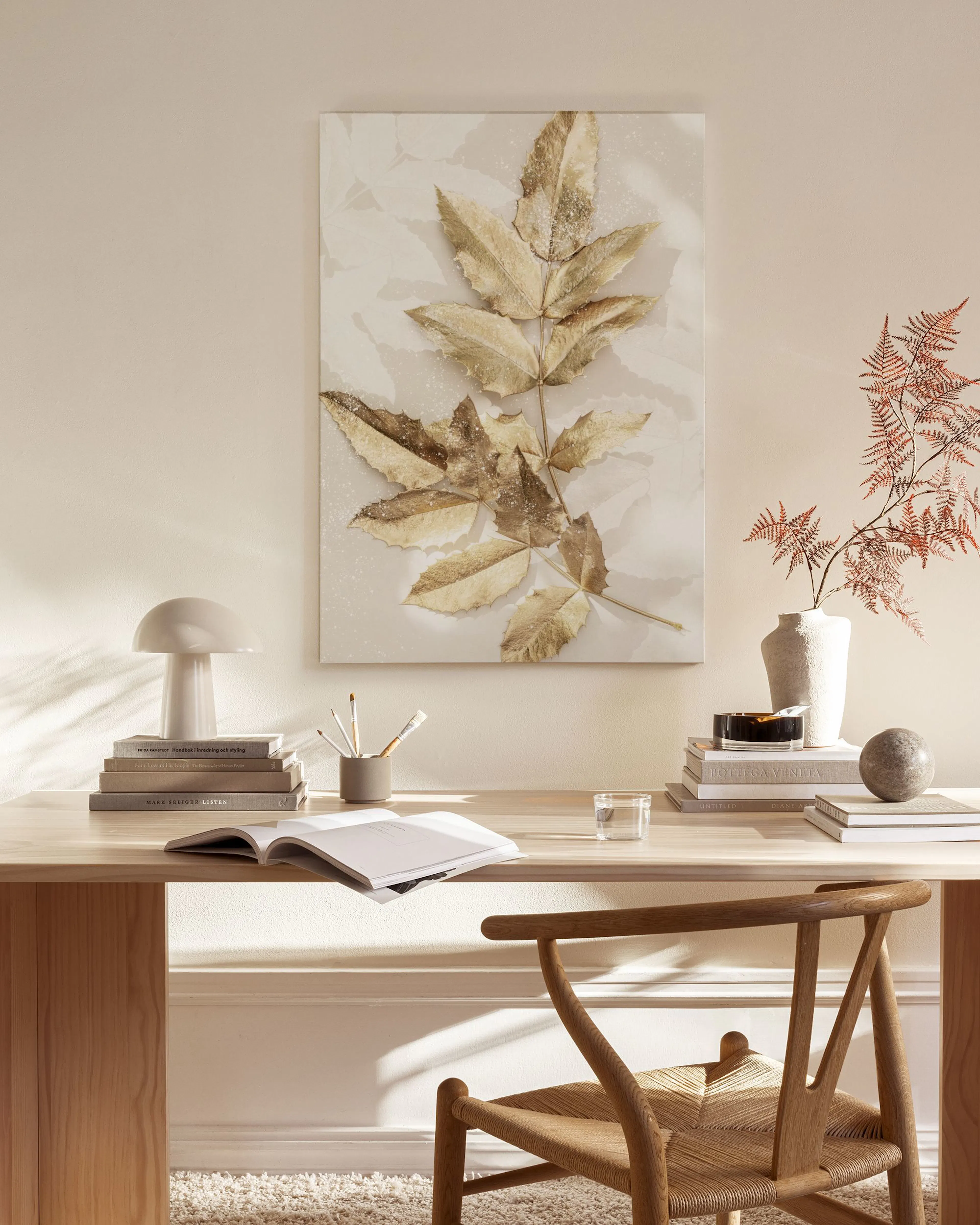 Lærred med guld- og bronzefarvede blade, ophængt i en minimalistisk stue med træmøbler og beige tæppe.