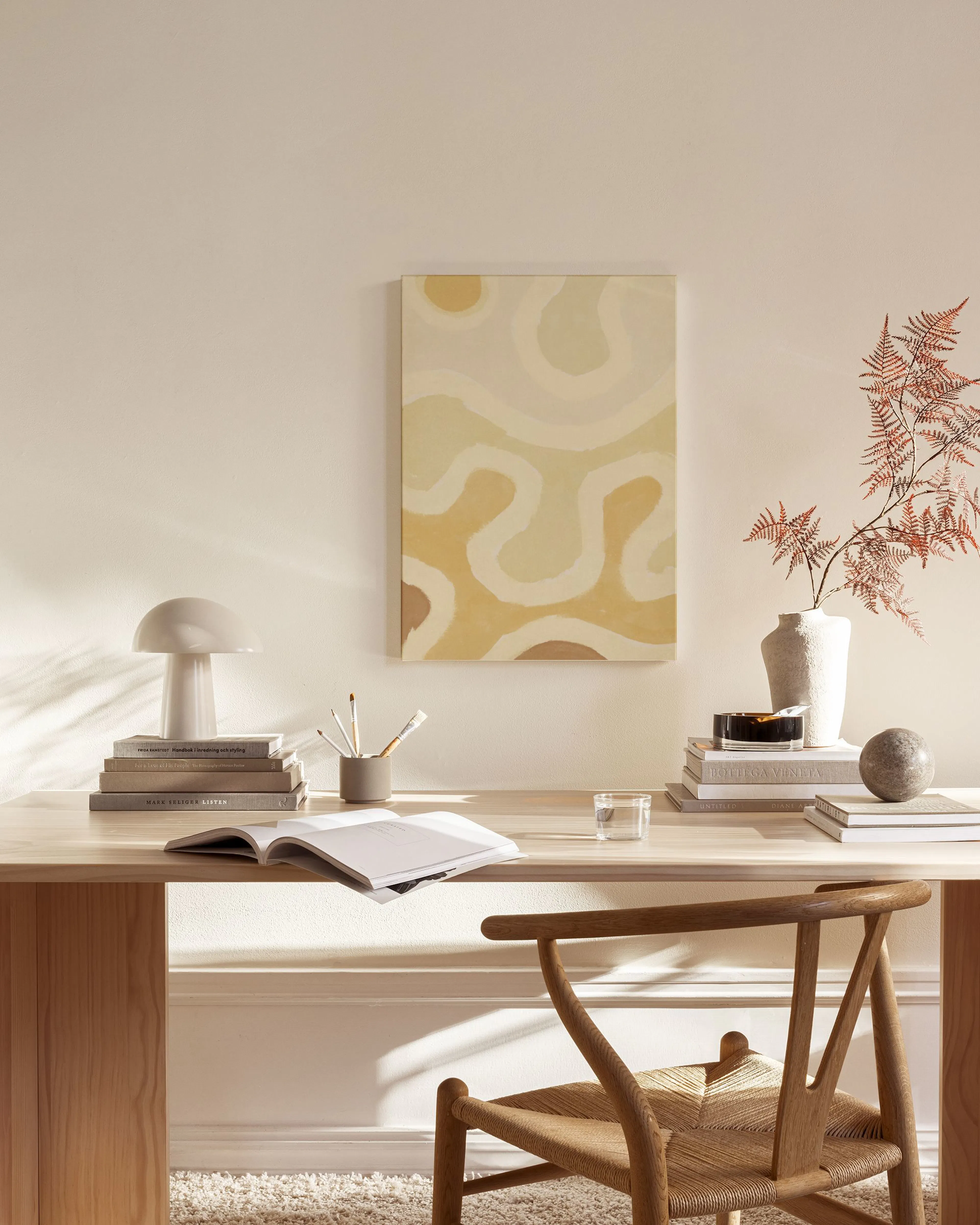 Leinwandbild mit organischen Formen in Beige- und Gelbtönen, in einem hellen Wohnzimmer über einer Kommode hängend.