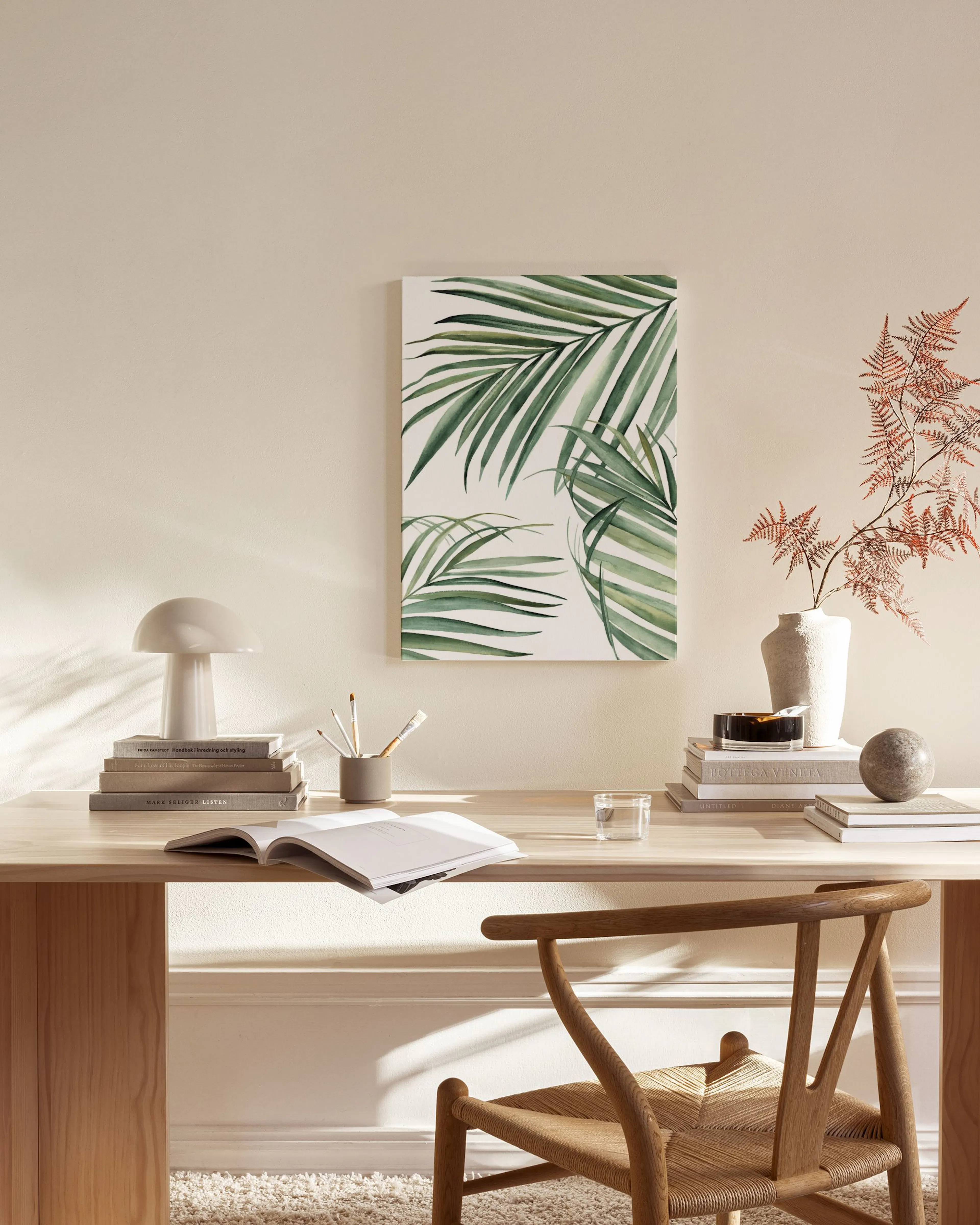 A canvas print of green palm leaves, displayed above a wooden console table in a light living room.