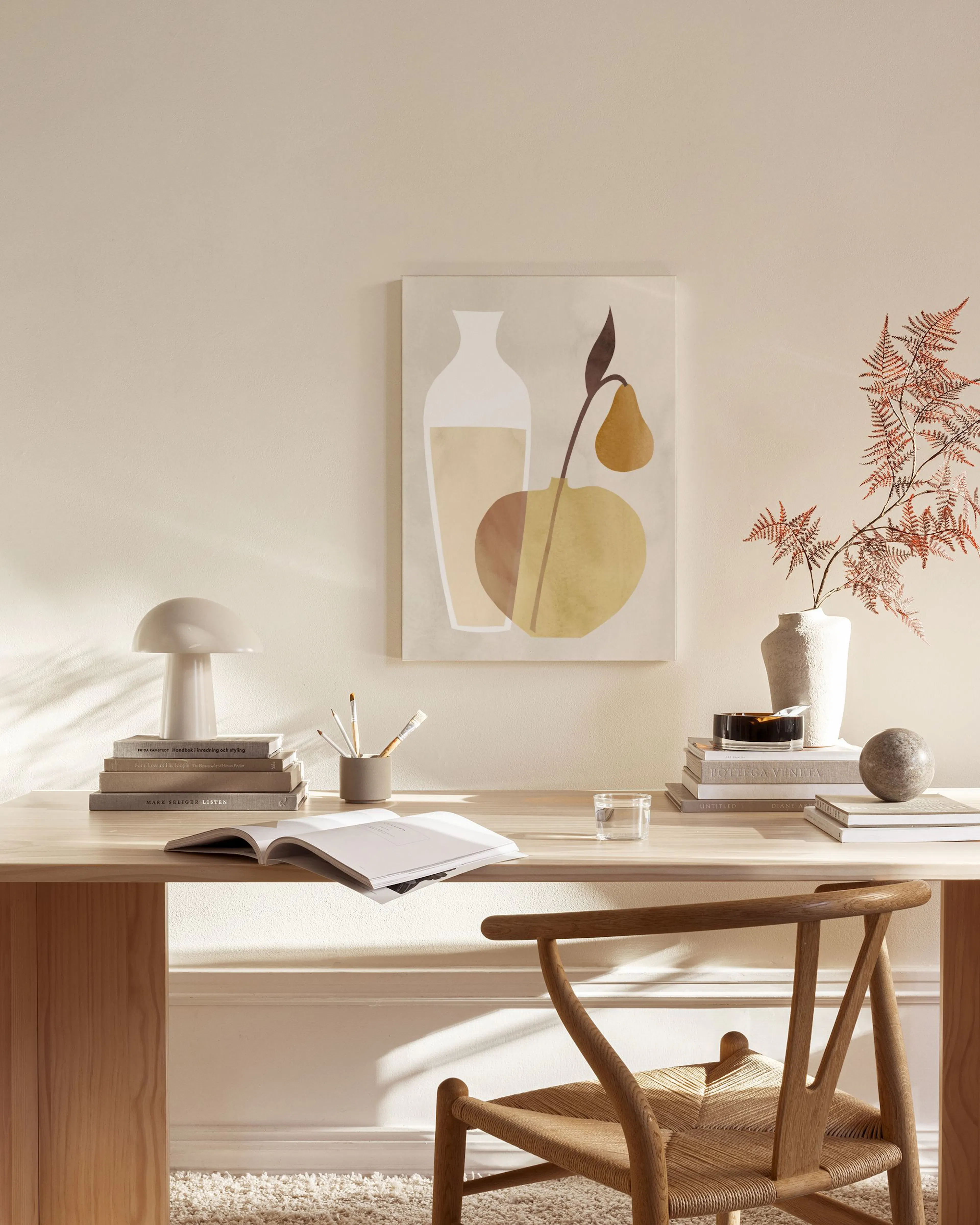 A minimalist still life print featuring a white vase and abstract fruit shapes in warm tones, hanging in a neutral living room.