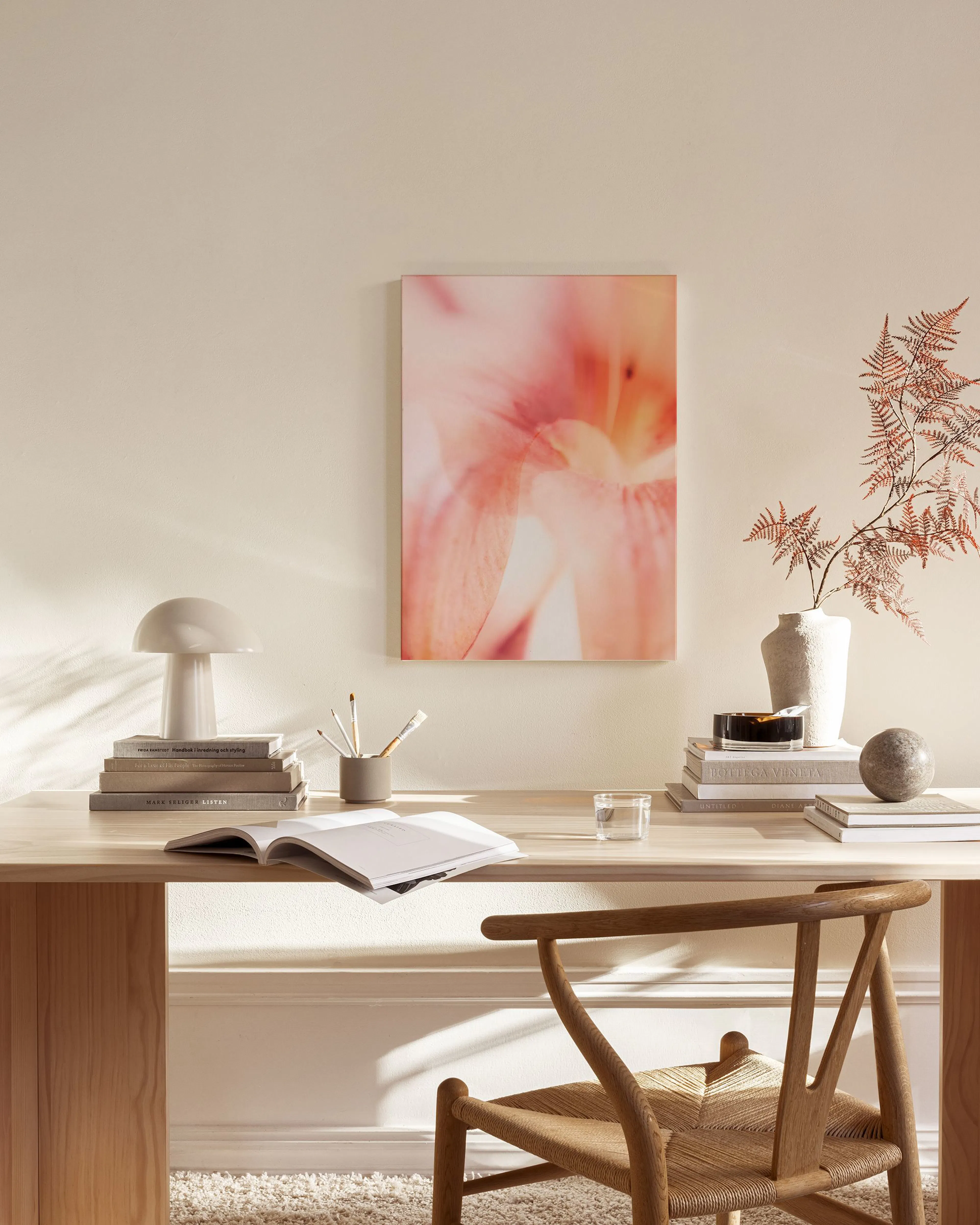 A canvas print of a soft pink flower with blurred petals, hanging above a light wood console table in a minimalist living room.