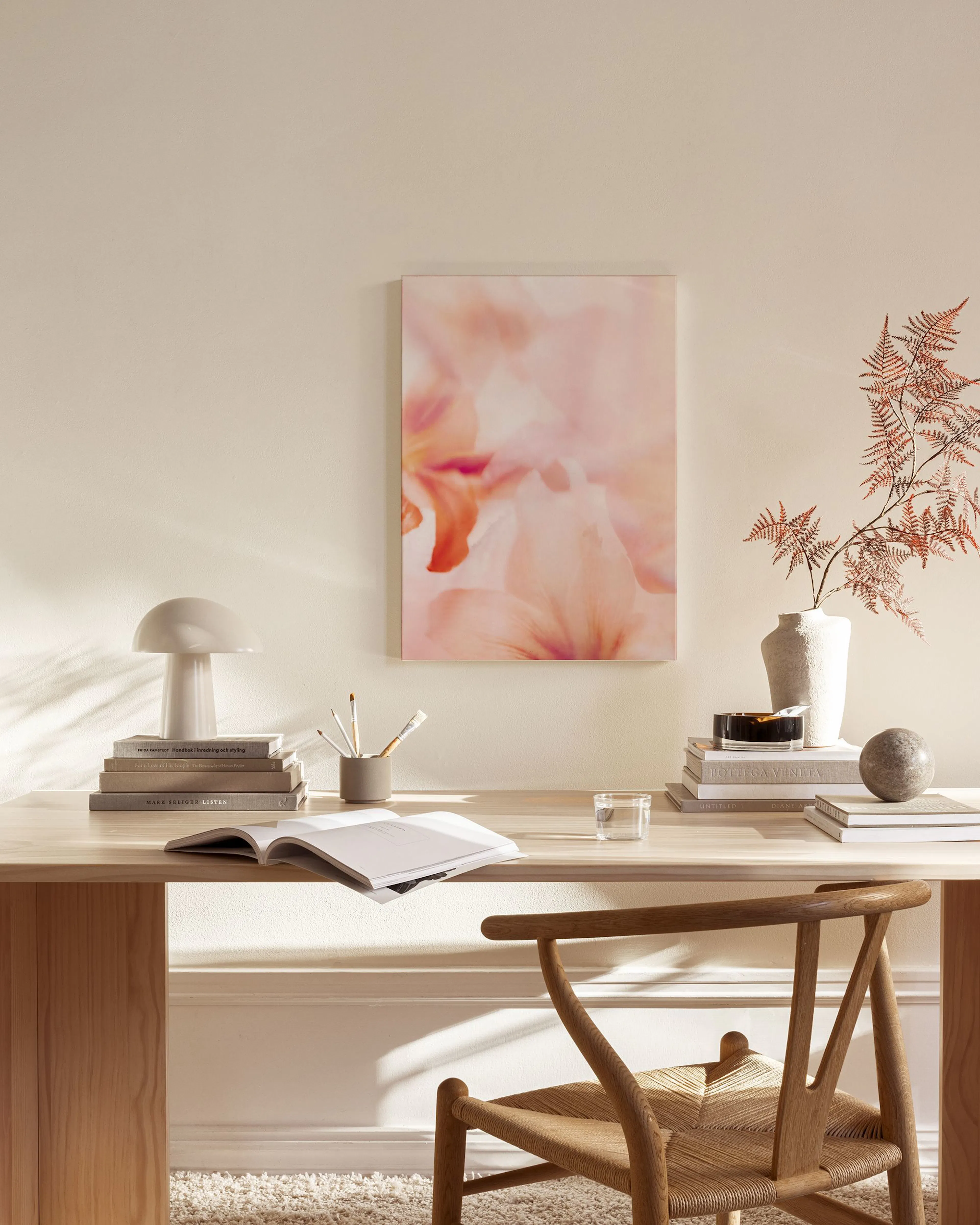 A canvas print of soft pink and orange floral blooms hanging on a cream wall above a timber console table in a modern living roo