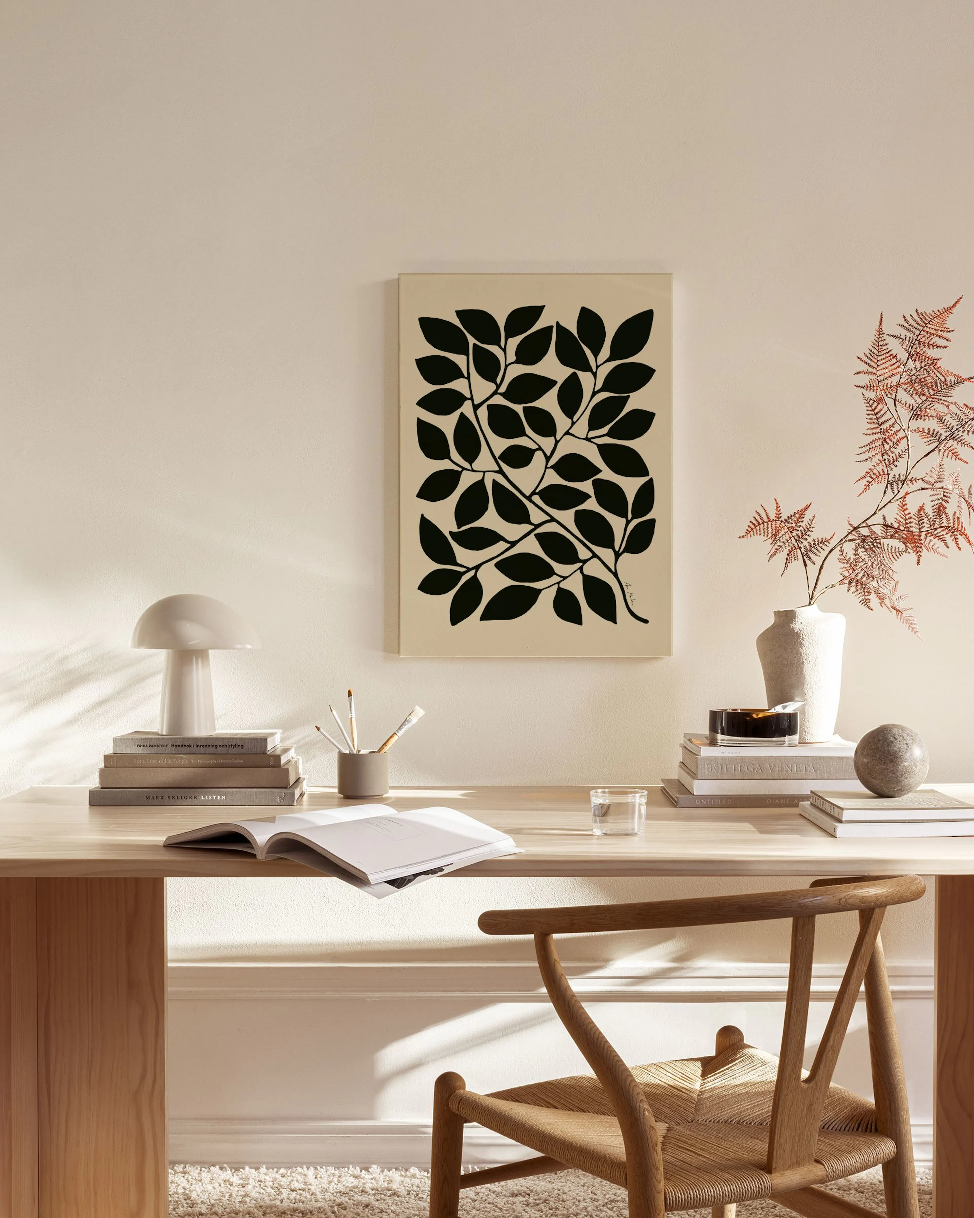 Toile murale minimaliste de feuilles noires sur fond beige, suspendue au-dessus dun banc en bois dans un salon lumineux.
