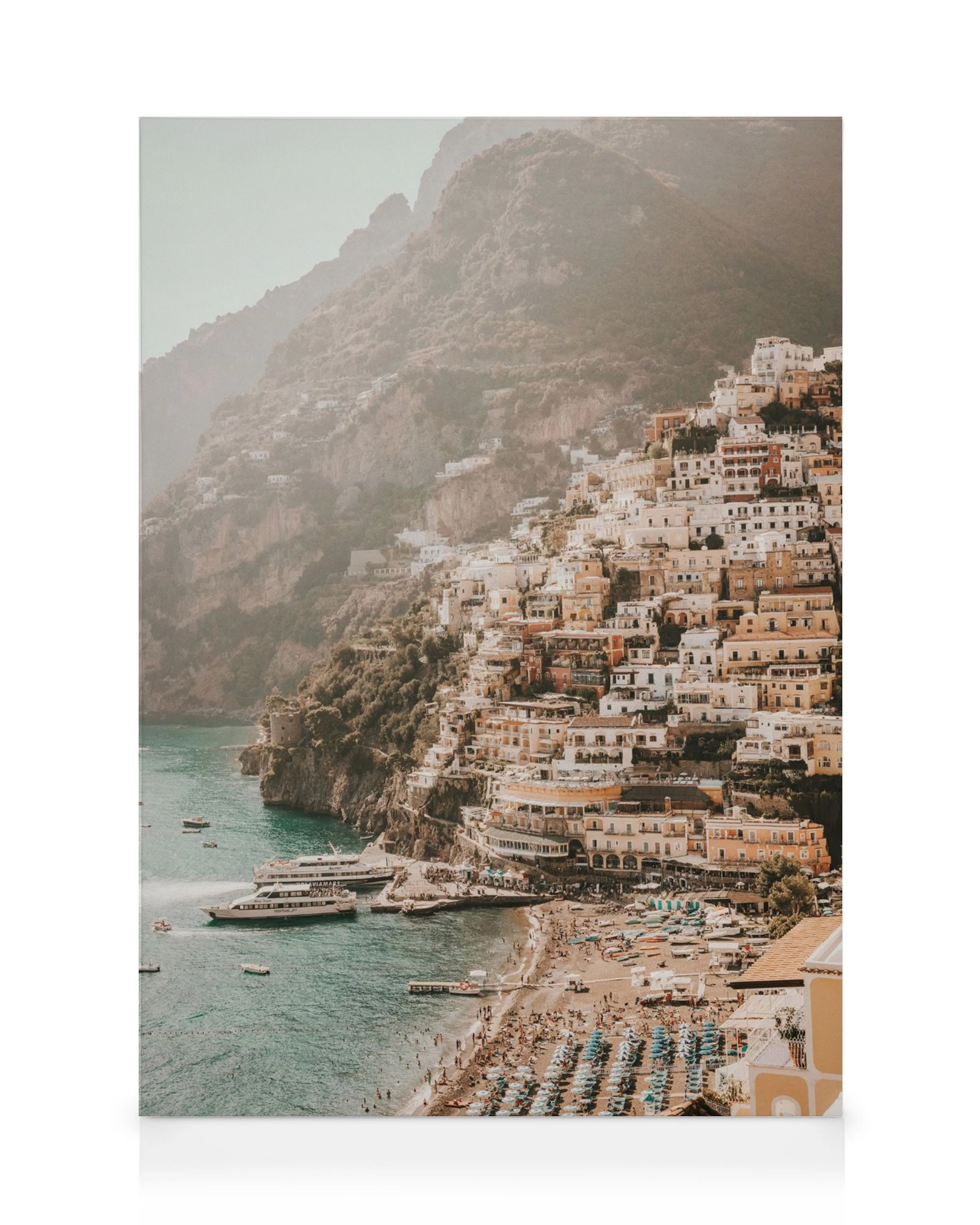 Stampa su tela di un villaggio mediterraneo con case colorate aggrappate a una scogliera, spiaggia e barche in mare.