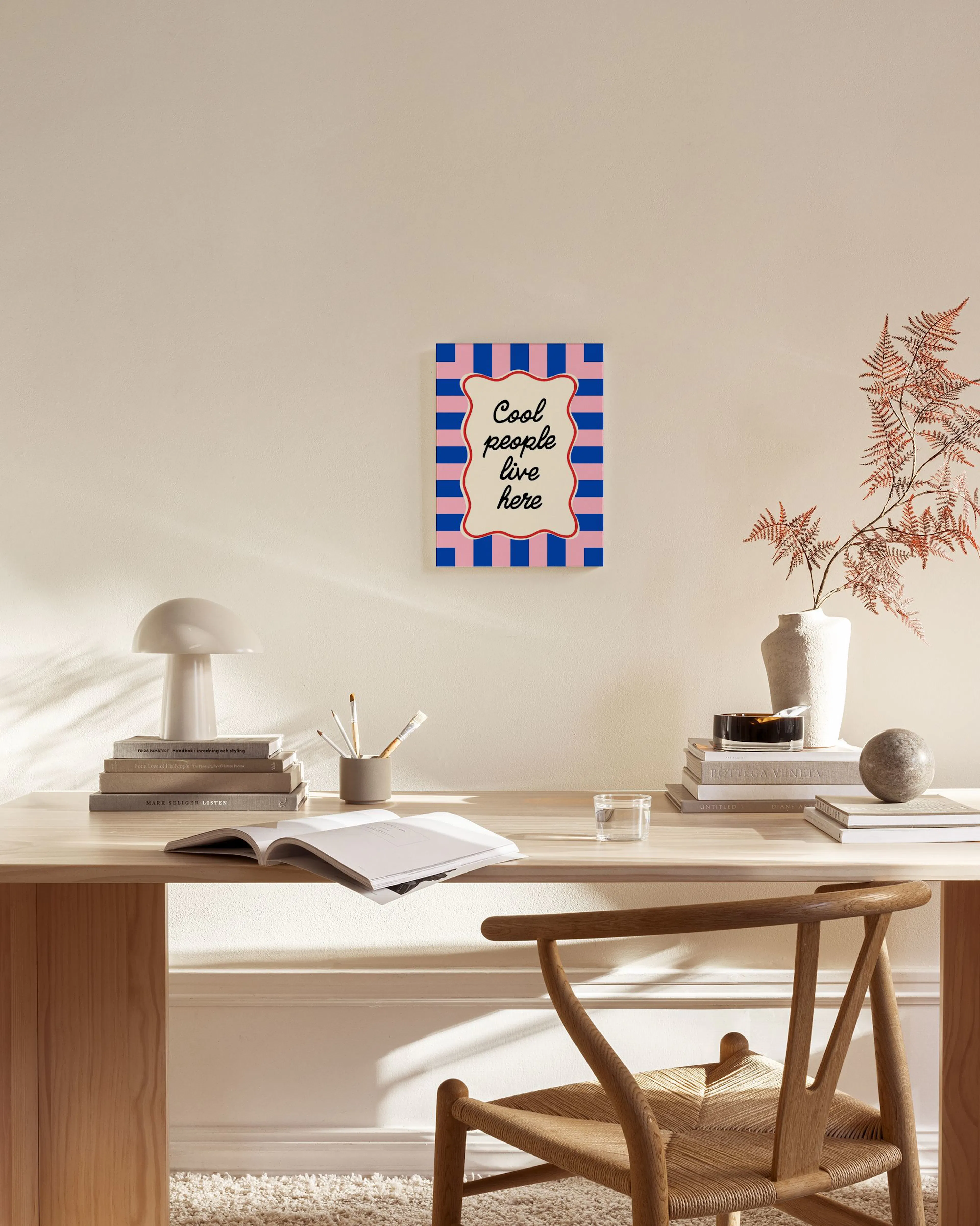 A canvas print with Cool people live here in black script on an off-white wavy shape, set against a pink and blue striped backgr