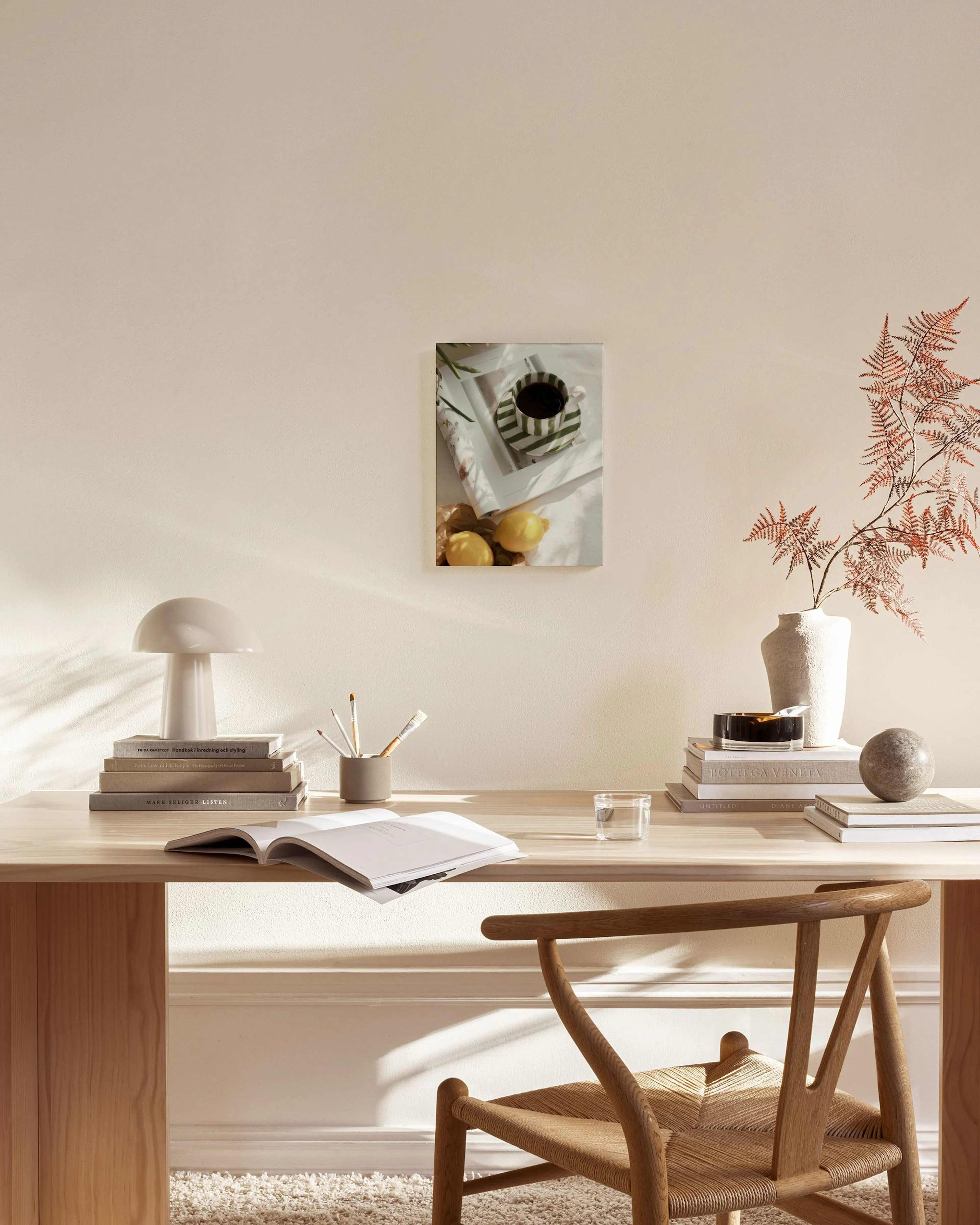 A canvas print showing a coffee cup with green and white stripes, a magazine, two lemons, and olive leaves on a white fabric sur