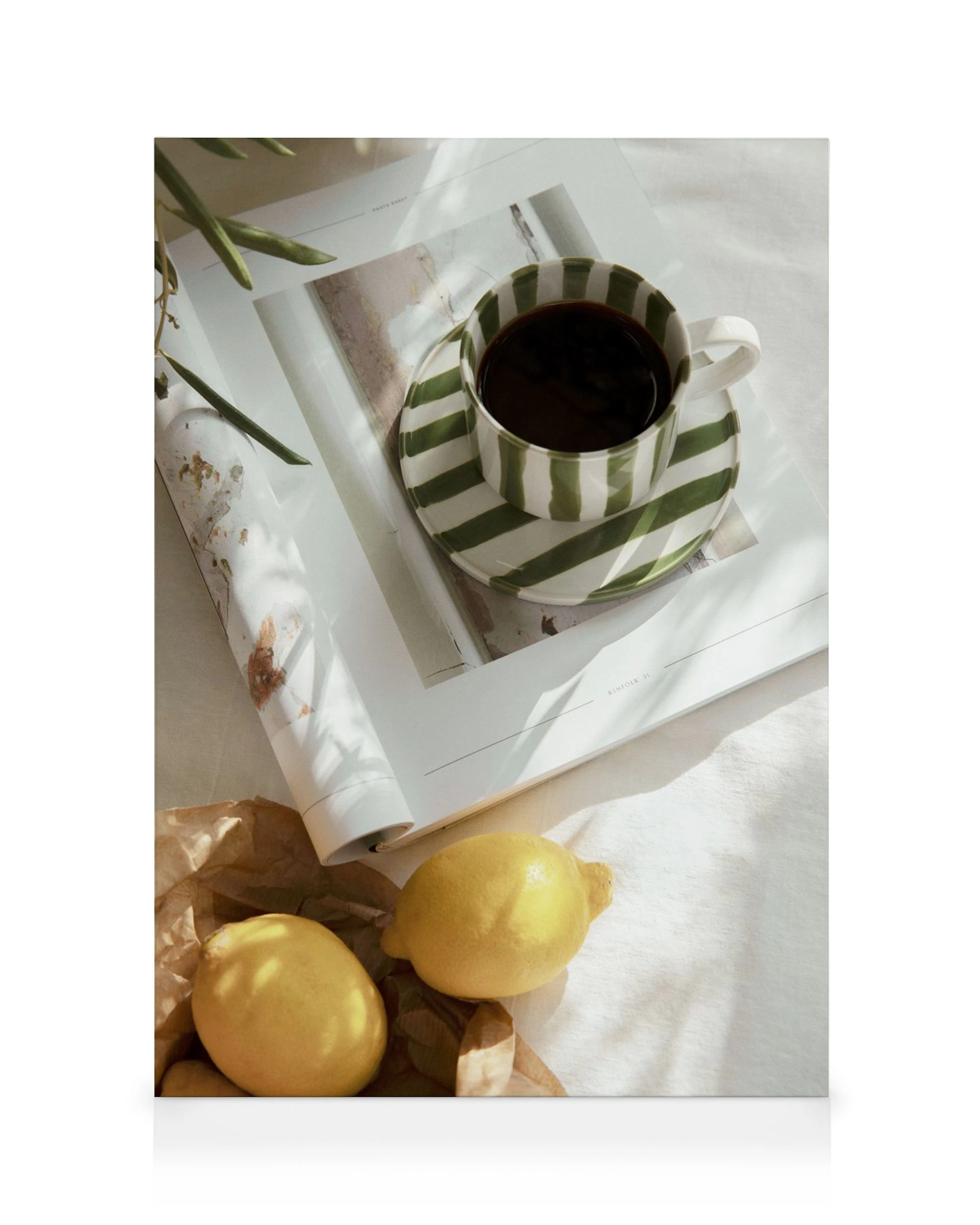 Stampa su tela di una tazza e piattino a strisce verdi e bianche con caffè su una rivista, due limoni e carta marrone.