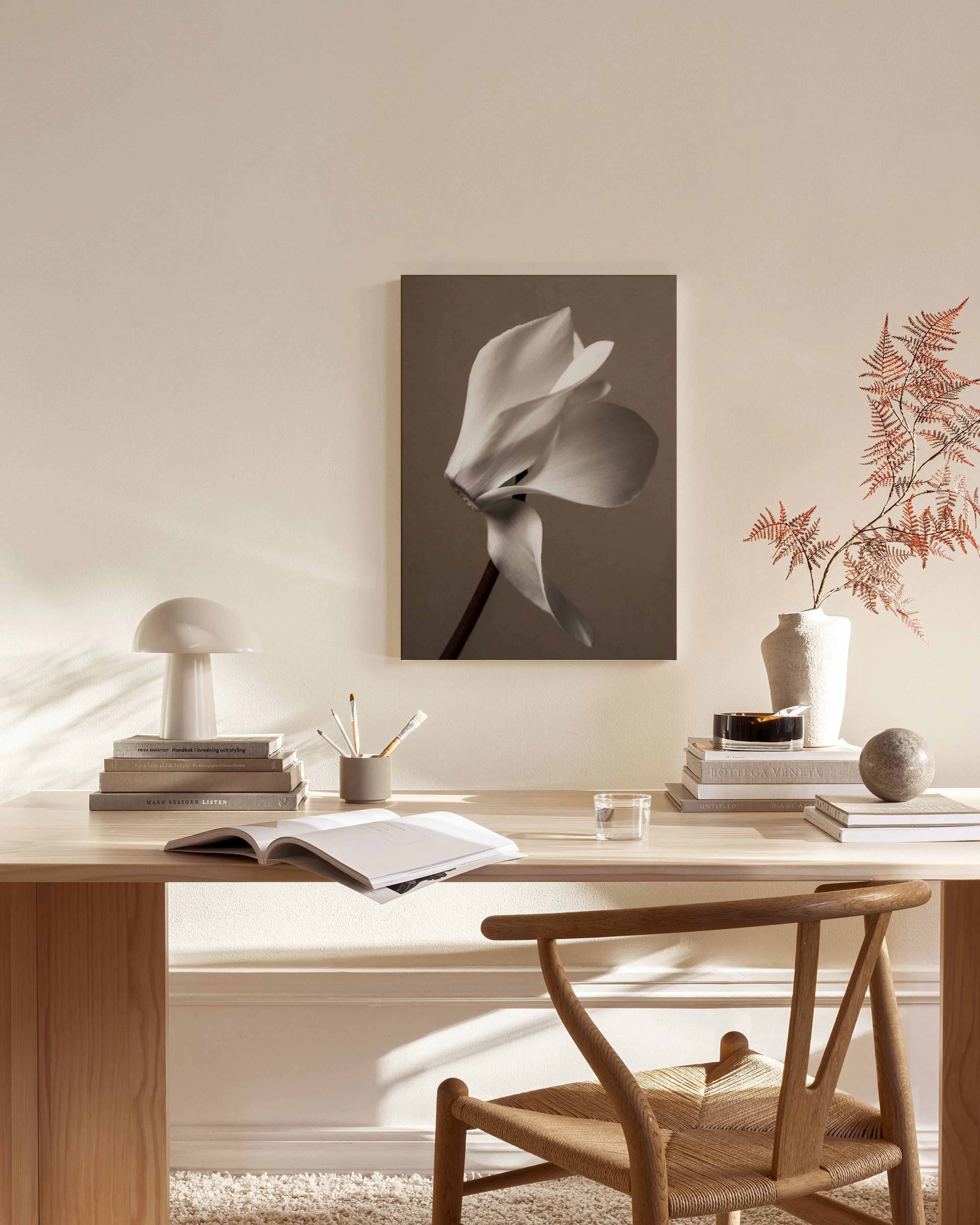 A canvas print of a white cyclamen flower on a brown background, displayed in a neutral-toned living room above a wooden console