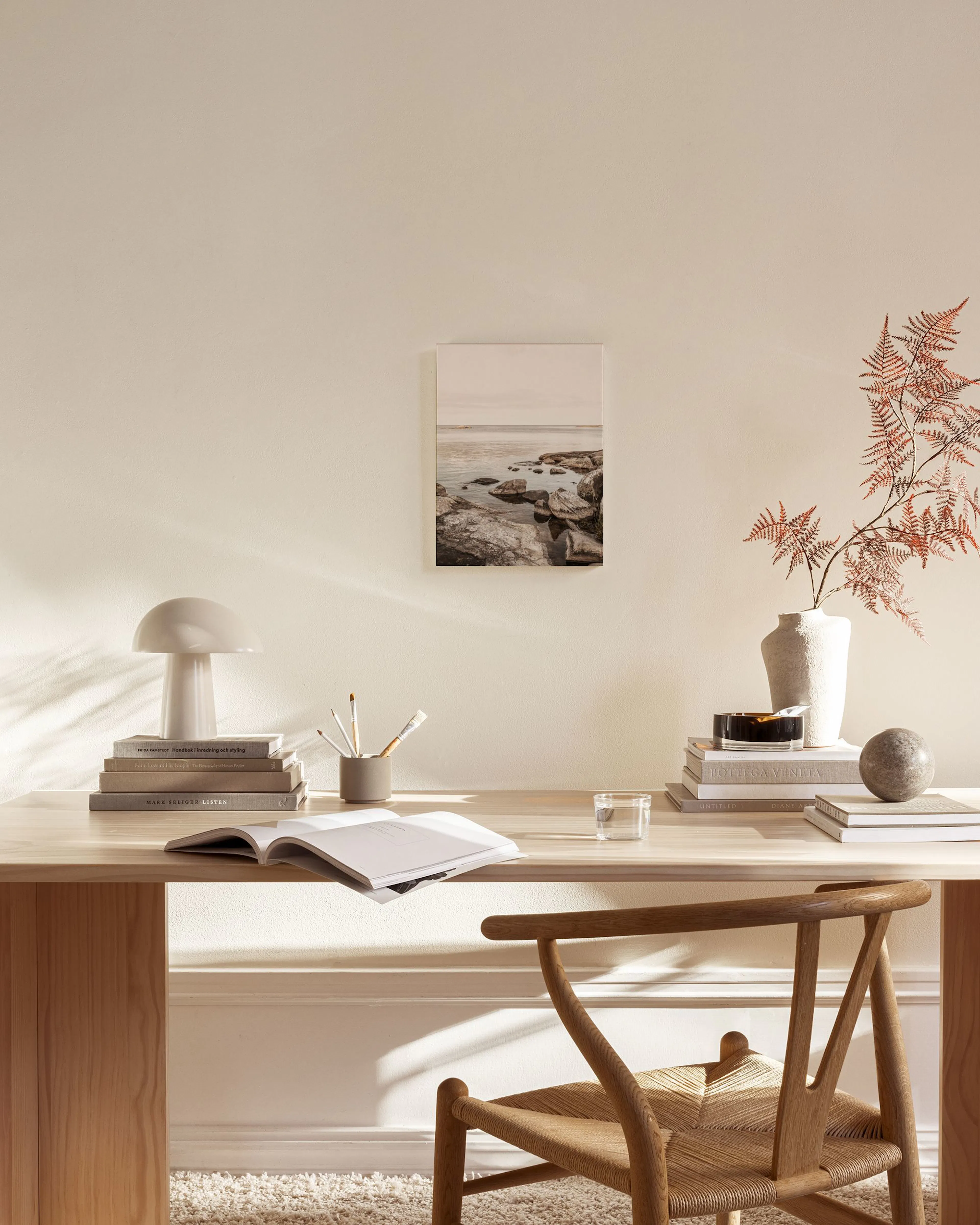 Canvas van een rotsachtige kustlijn en kalme zee, hangend in een lichte woonkamer boven een houten dressoir.