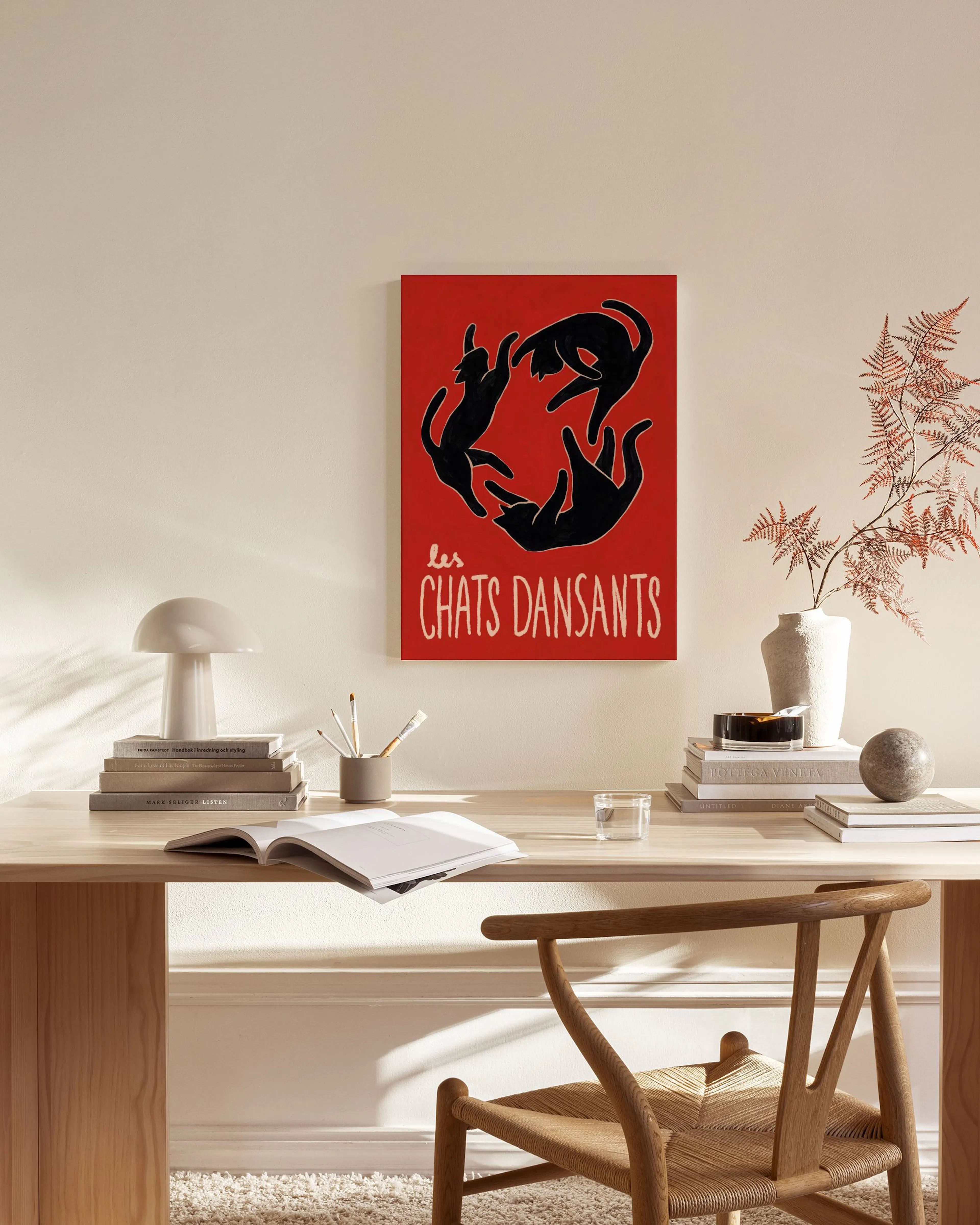 Canvastavla med tre svarta katter som dansar i en cirkel mot röd bakgrund, i ett ljust vardagsrum.