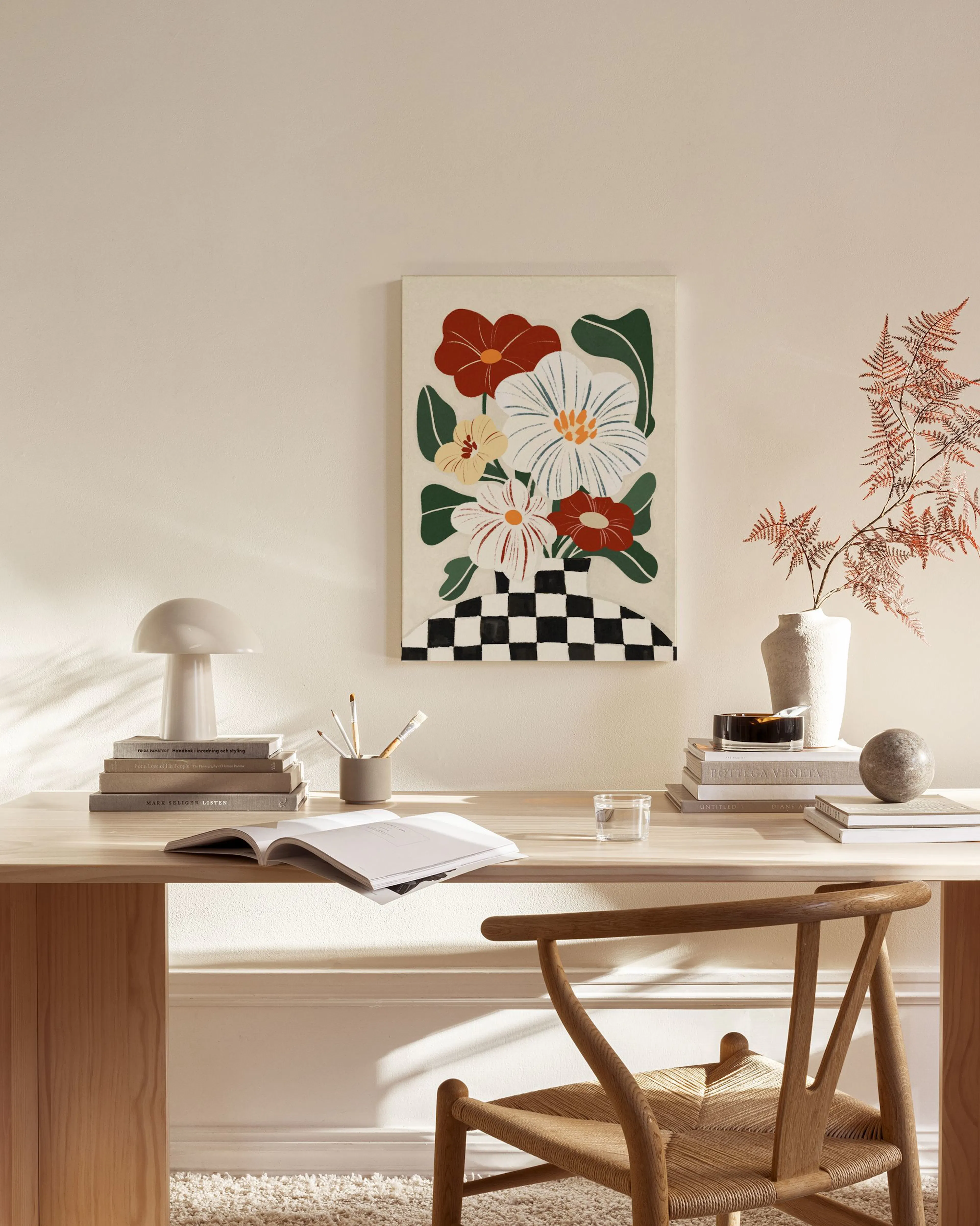 Lærred med farverige blomsterbuket i rød, hvid og gul i en sort-hvid ternet vase, hængende i en stue.