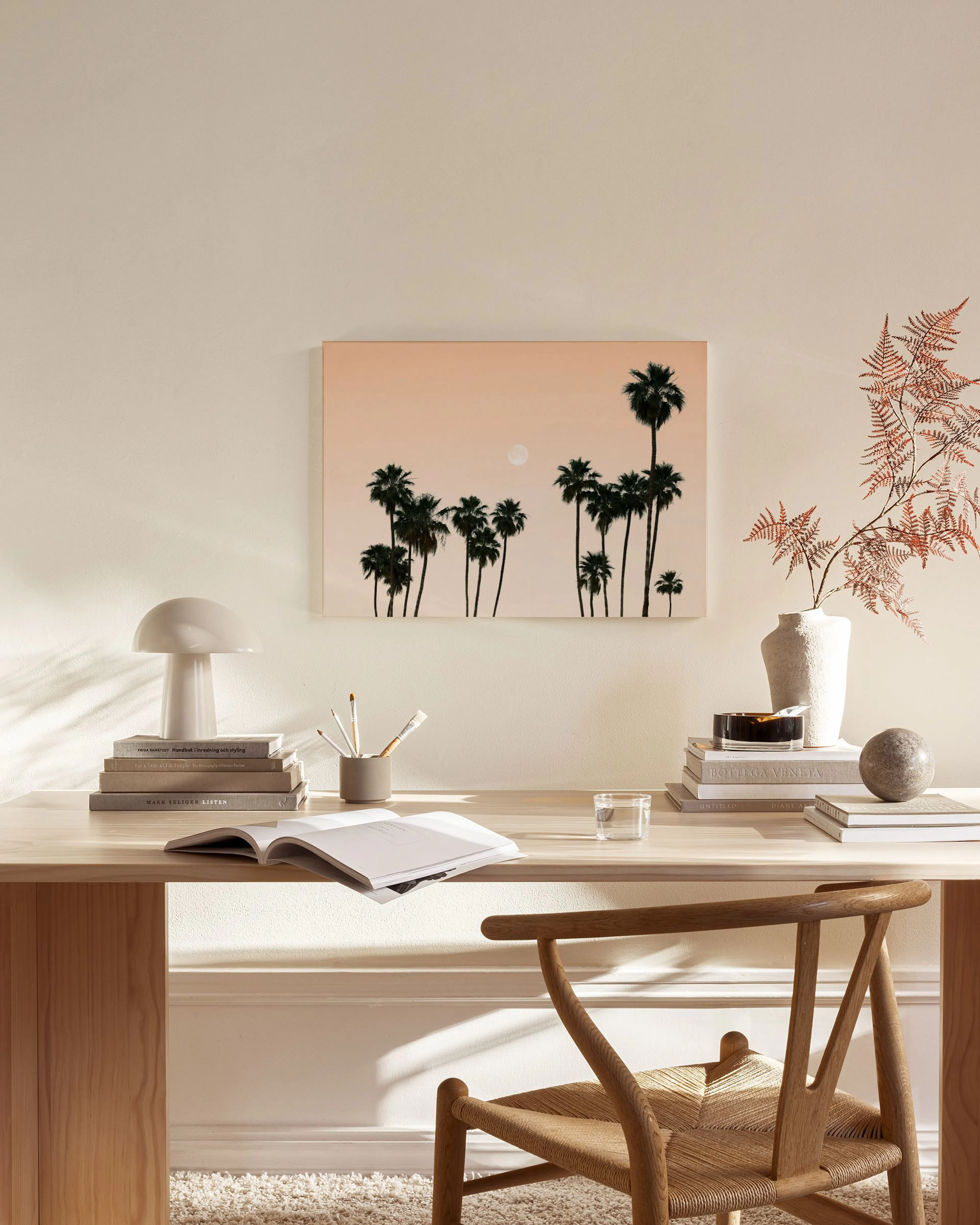 Canvas met zwarte palmbomen en volle maan tegen een oranje hemel, hangend in een moderne woonkamer.
