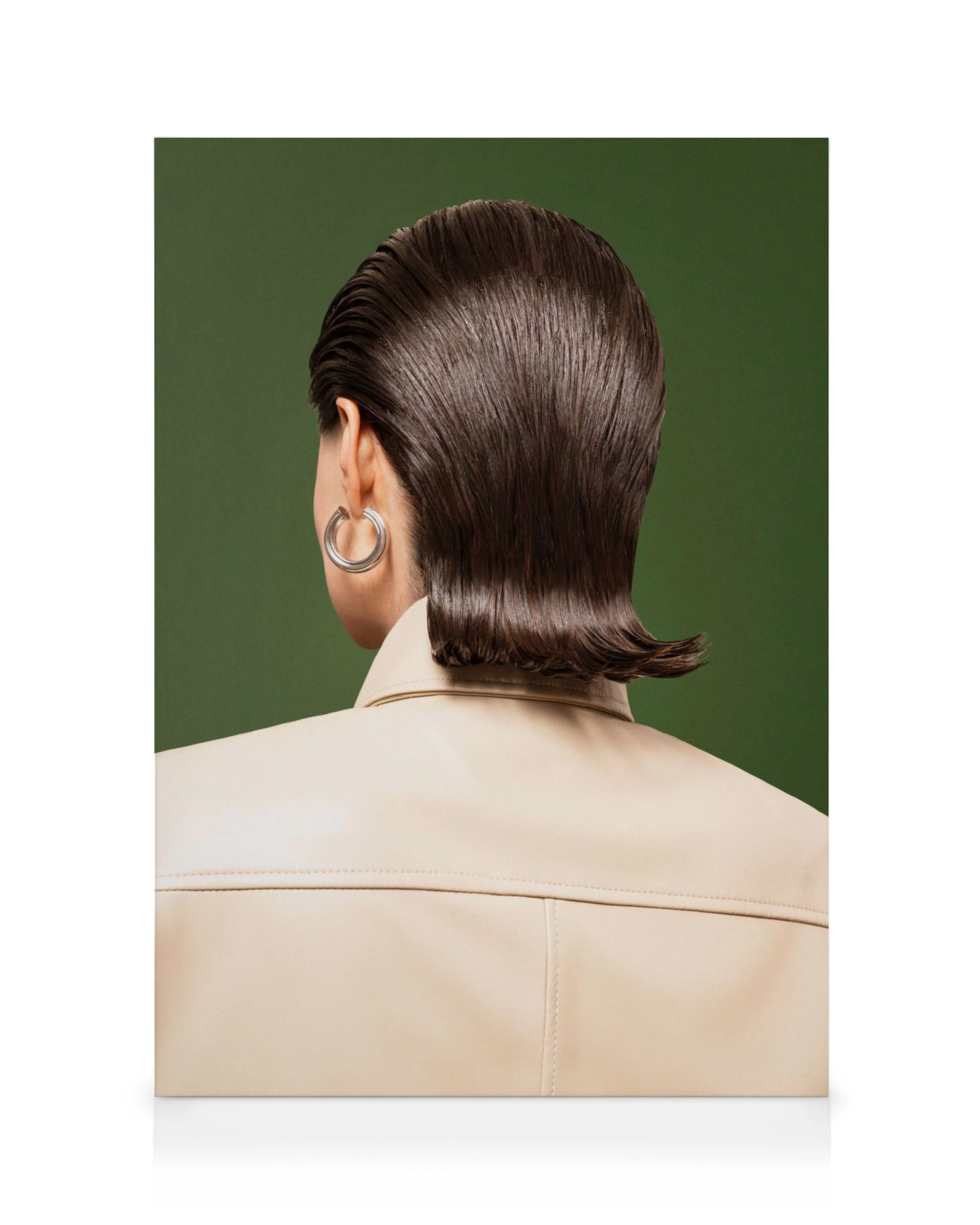 Toile de femme brune avec une coiffure chic effet mouillé, portant une veste beige et une boucle doreille argentée