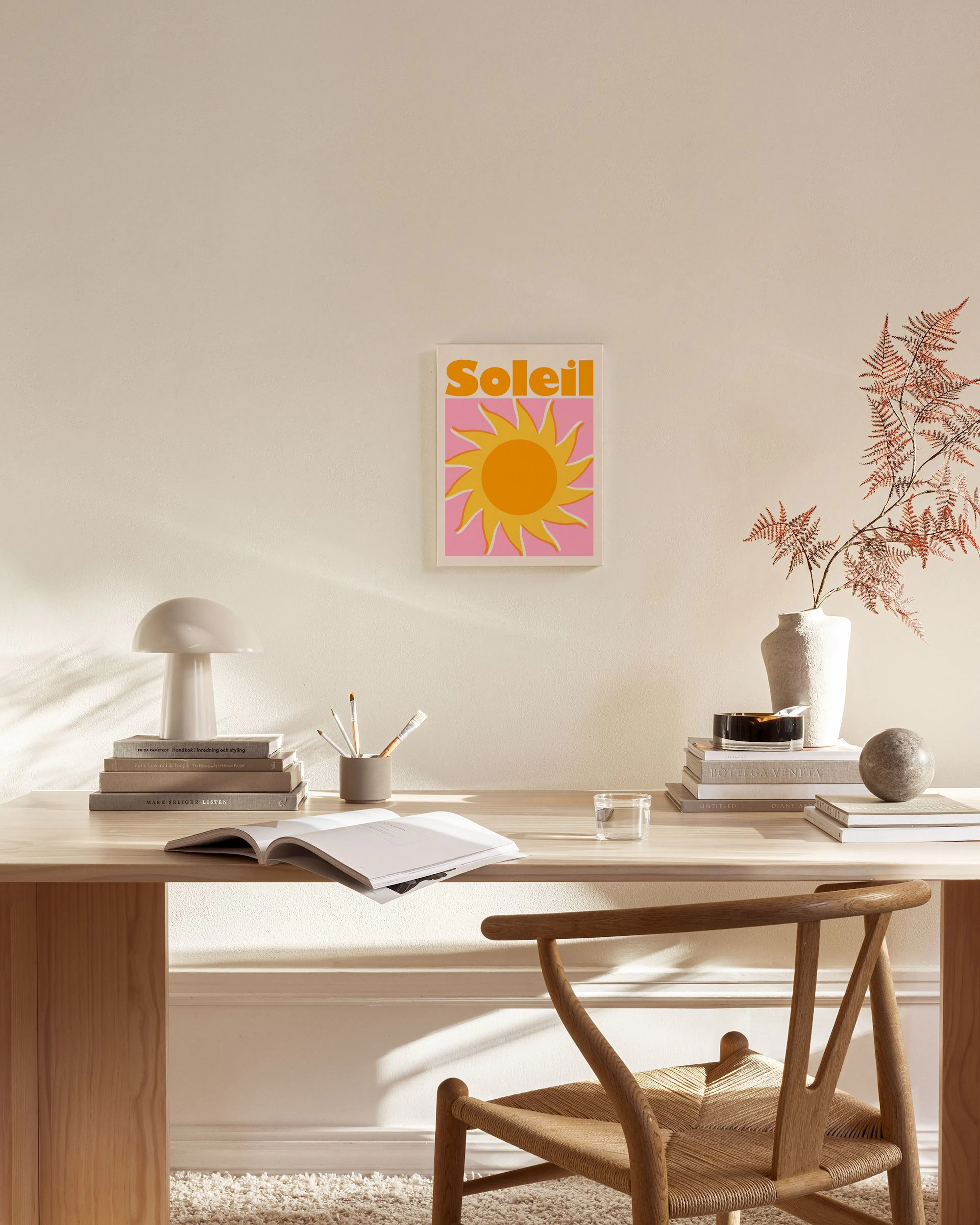 A canvas print with a yellow sun and pink rays, above the word Soleil in orange, hanging in a light living room.
