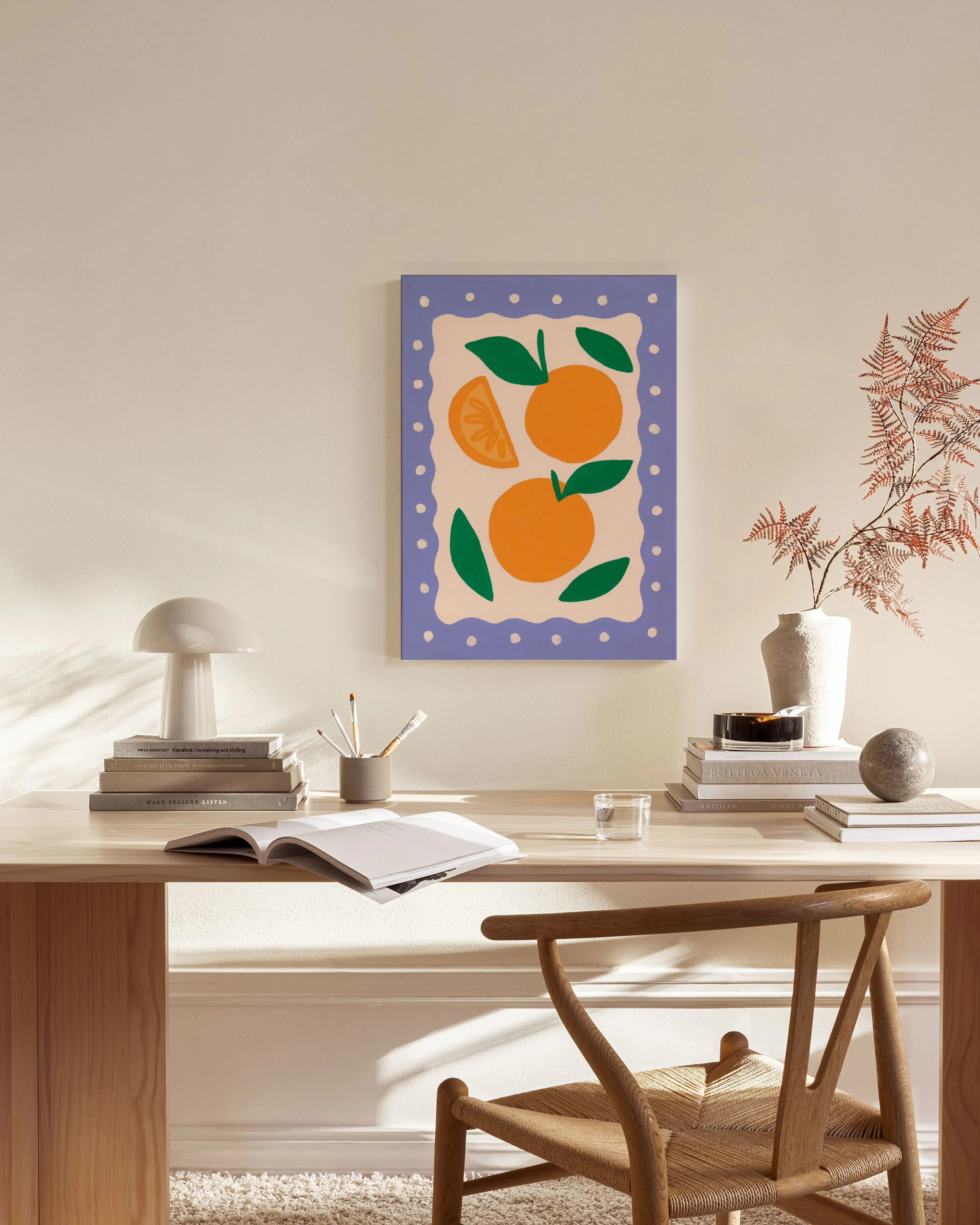 An orange fruit print with green leaves and a scalloped purple border, hanging in a minimalist living room.